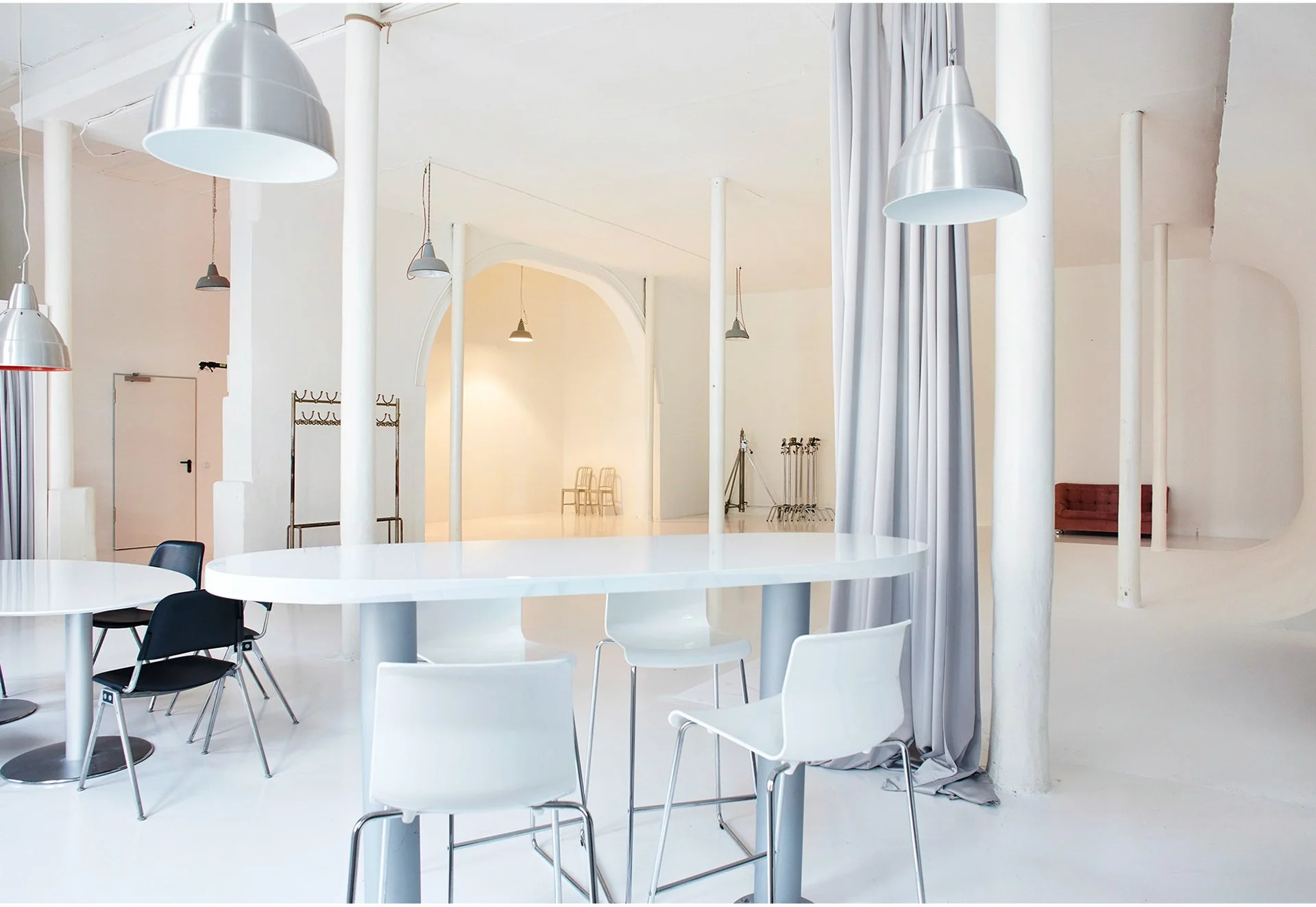 Ein moderner, heller Raum mit weißen Wänden und mehreren Stühlen und Tischen in Schwarz und Weiß, sowie großen Lampen an der Decke.