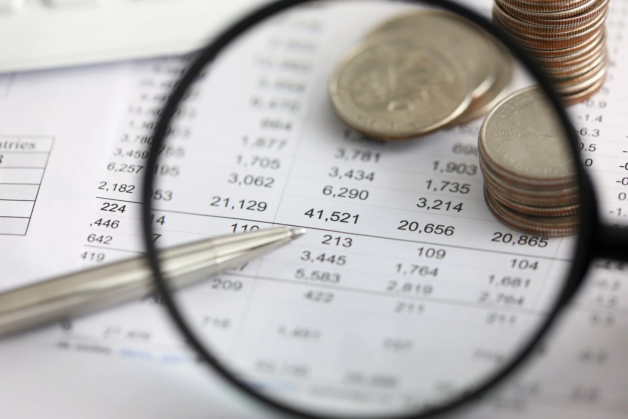 Close-up of pennies and coins stacked on financial documents, seen through a magnifying glass.