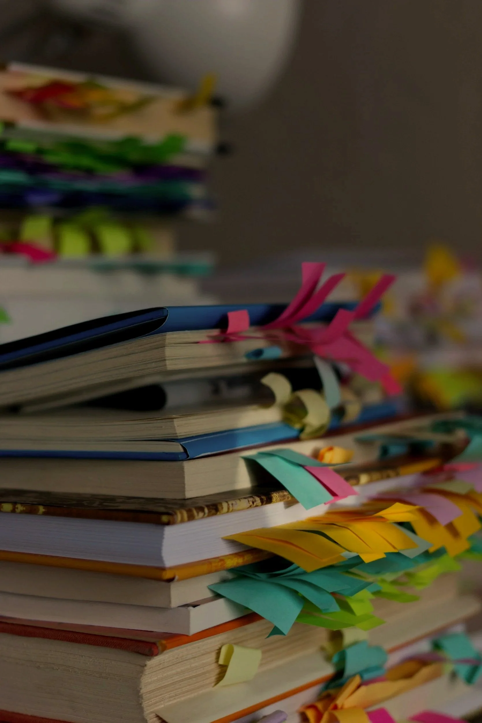 A stack of books with colorful sticky notes protruding from the pages, placed on a desk.