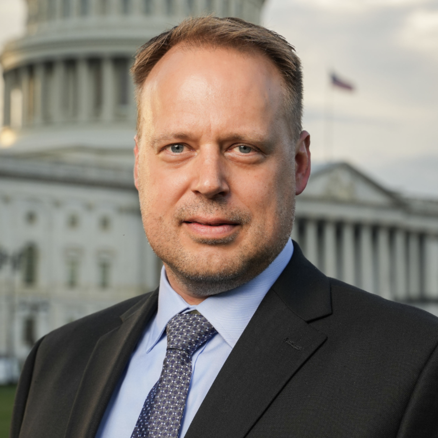 A man in a suit and tie standing outdoors with the U.S. Capitol in the background.