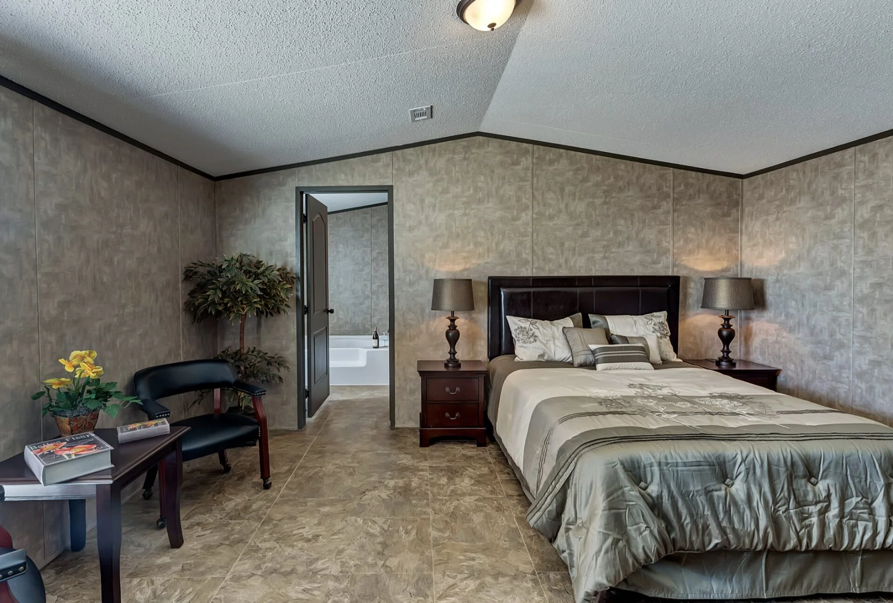 A bedroom with a bed, nightstands, lamps, and a doorway leading to a bathroom with a bathtub.