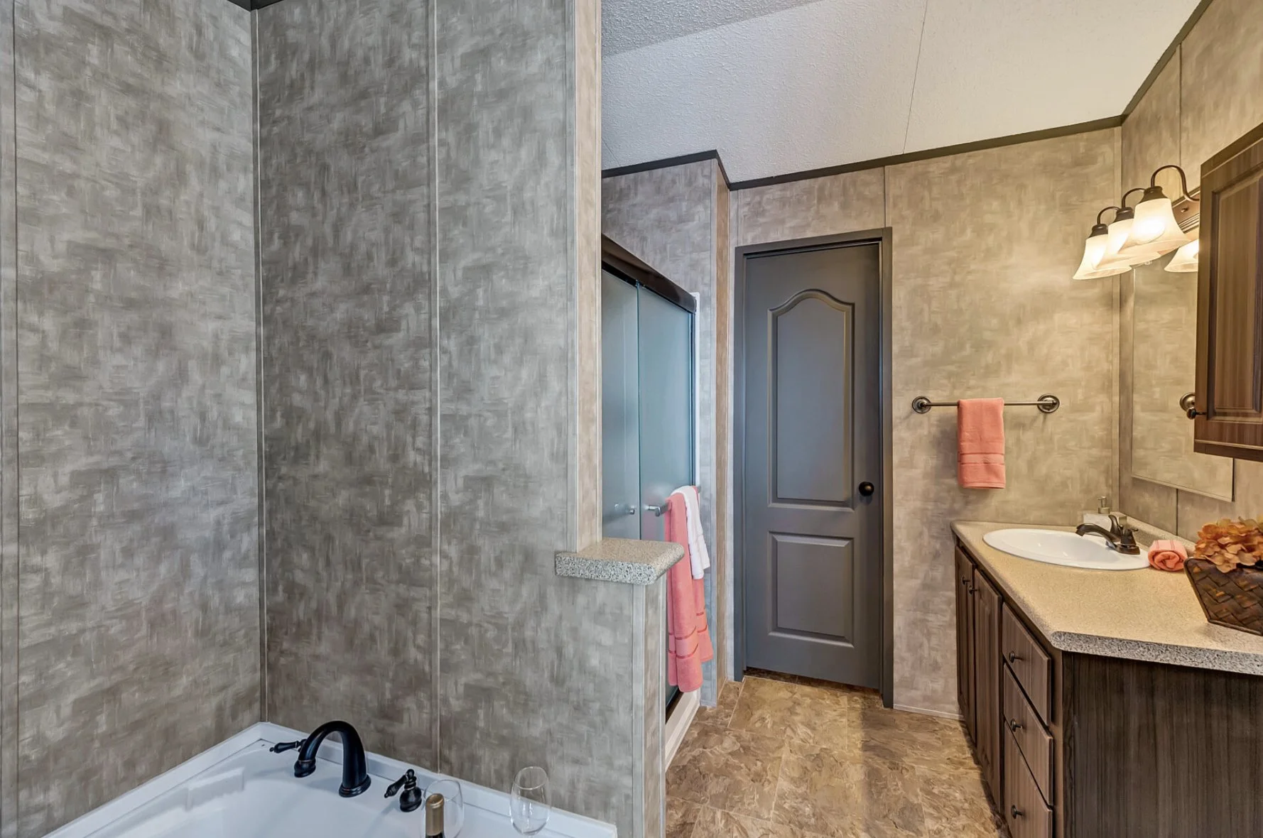 Bathroom with a shower, bathtub, gray door, wooden vanity with a sink, pink towels, and a mirror and light fixture above the sink.