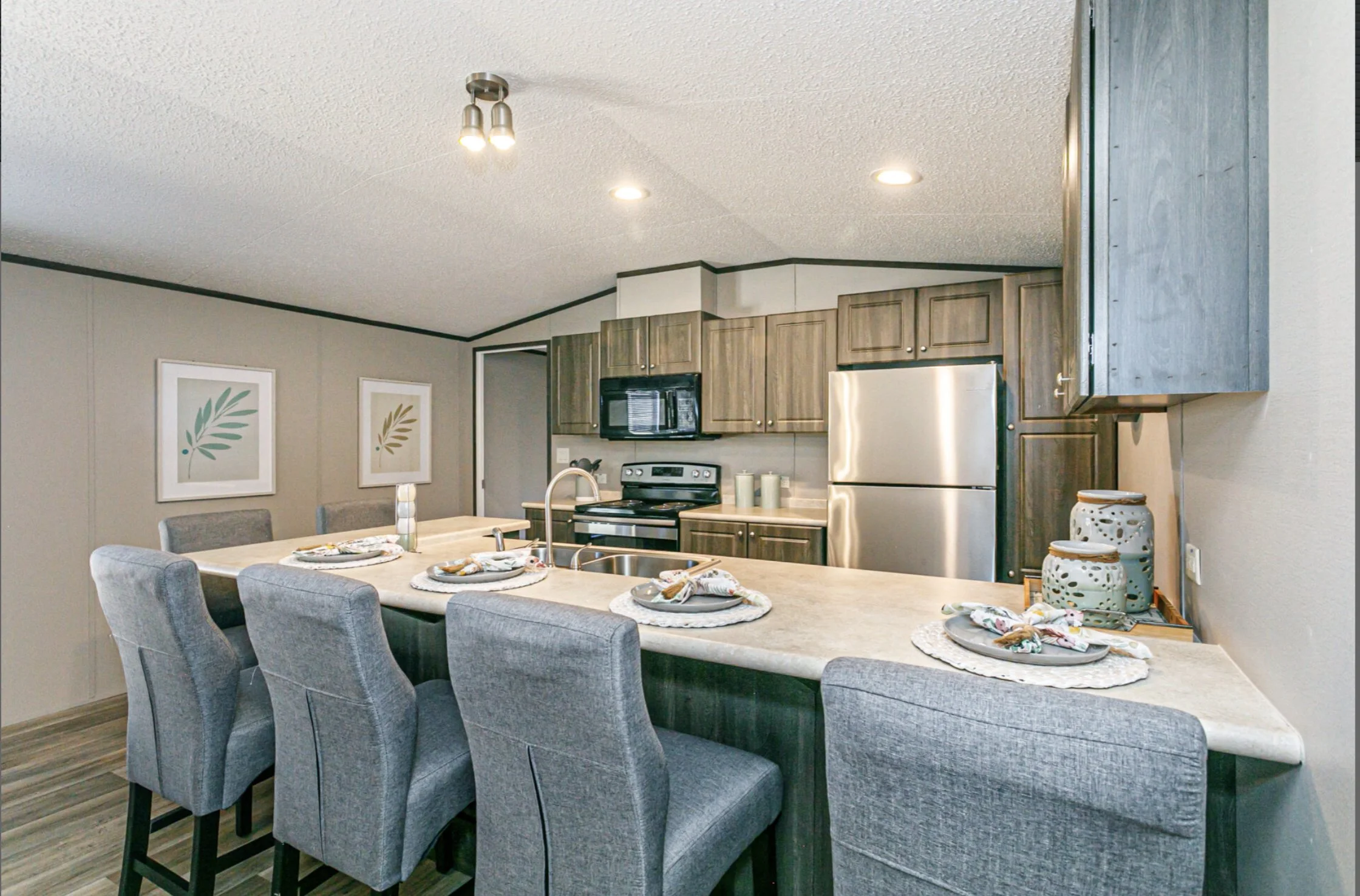 Kitchen with gray chairs around a light-colored island, wooden cabinets, stainless steel appliances, and decorative table settings.
