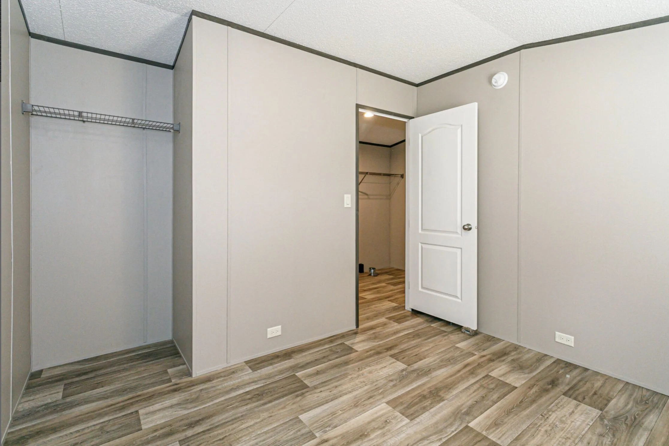 Empty room with beige walls, wooden flooring, an open closet, and a closed white door.