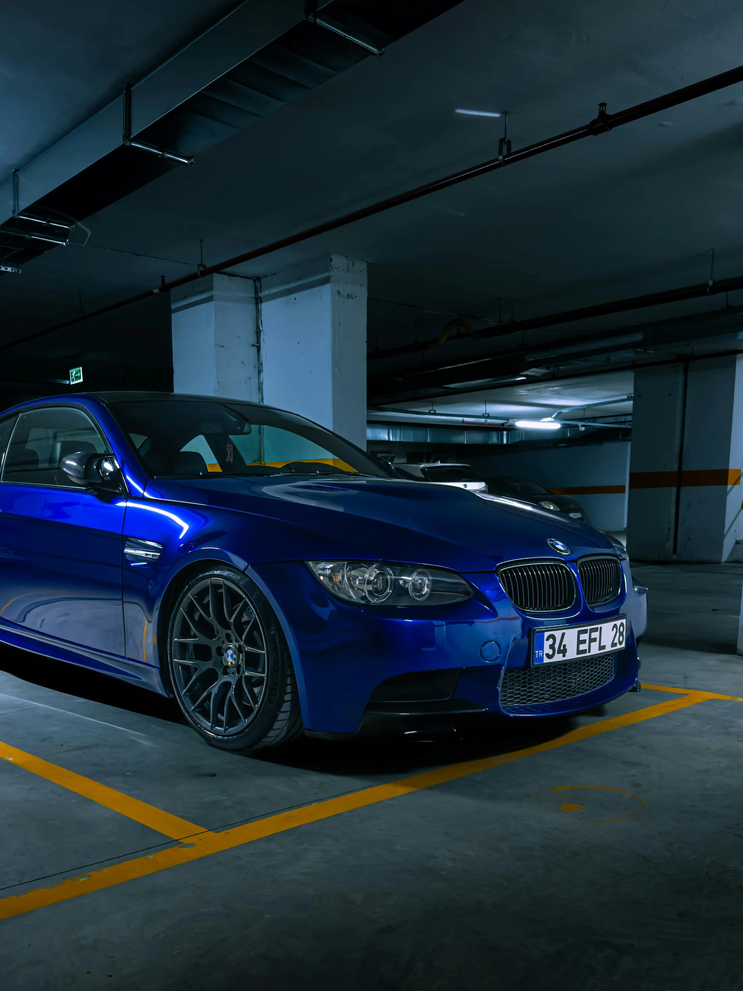 A blue BMW car parked in an underground parking garage with dim lighting and concrete structures.