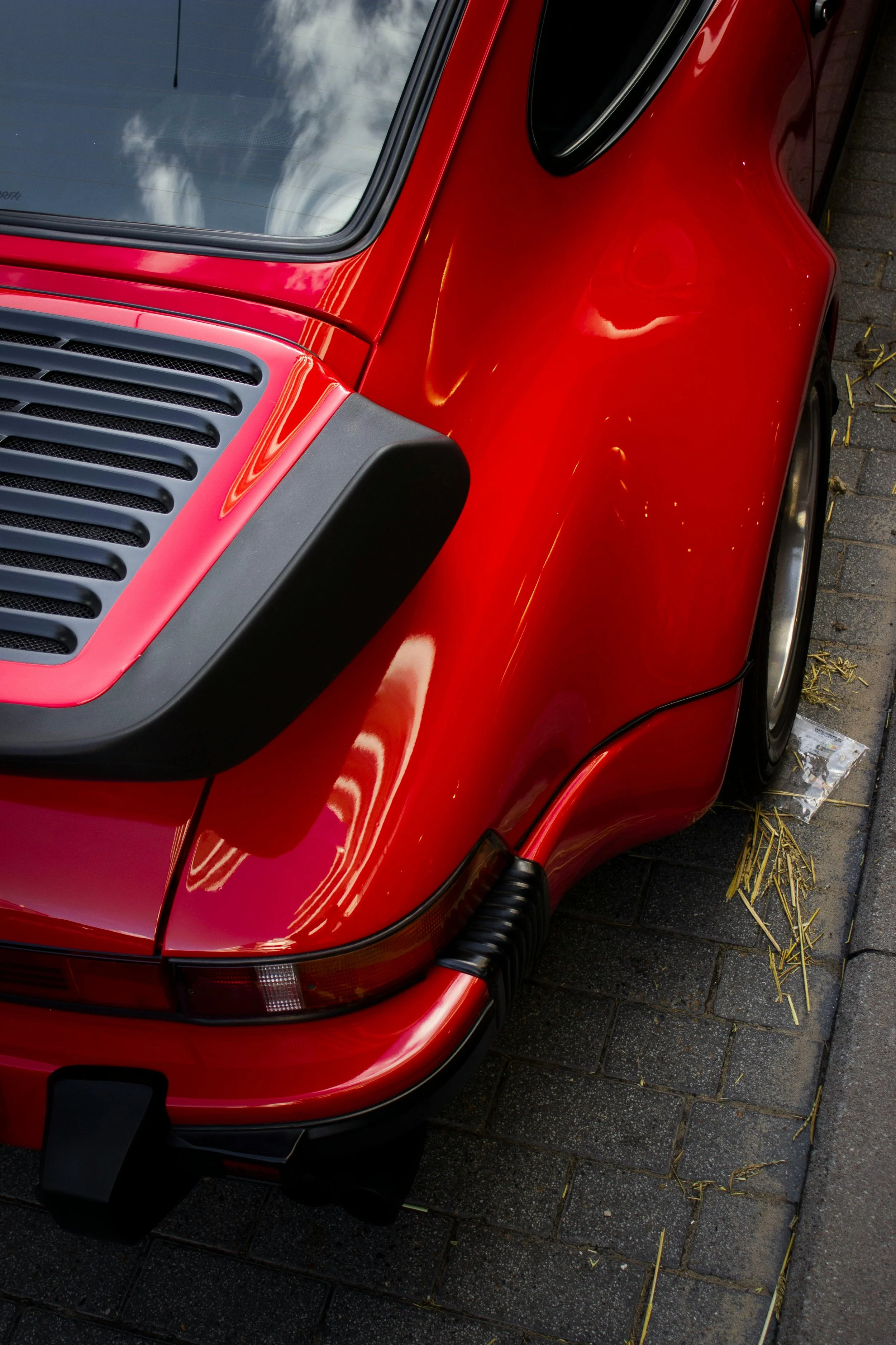 Close-up of the front left side of a red sports car parked on a street with a view of the windshield, hood, headlight, and wheel.