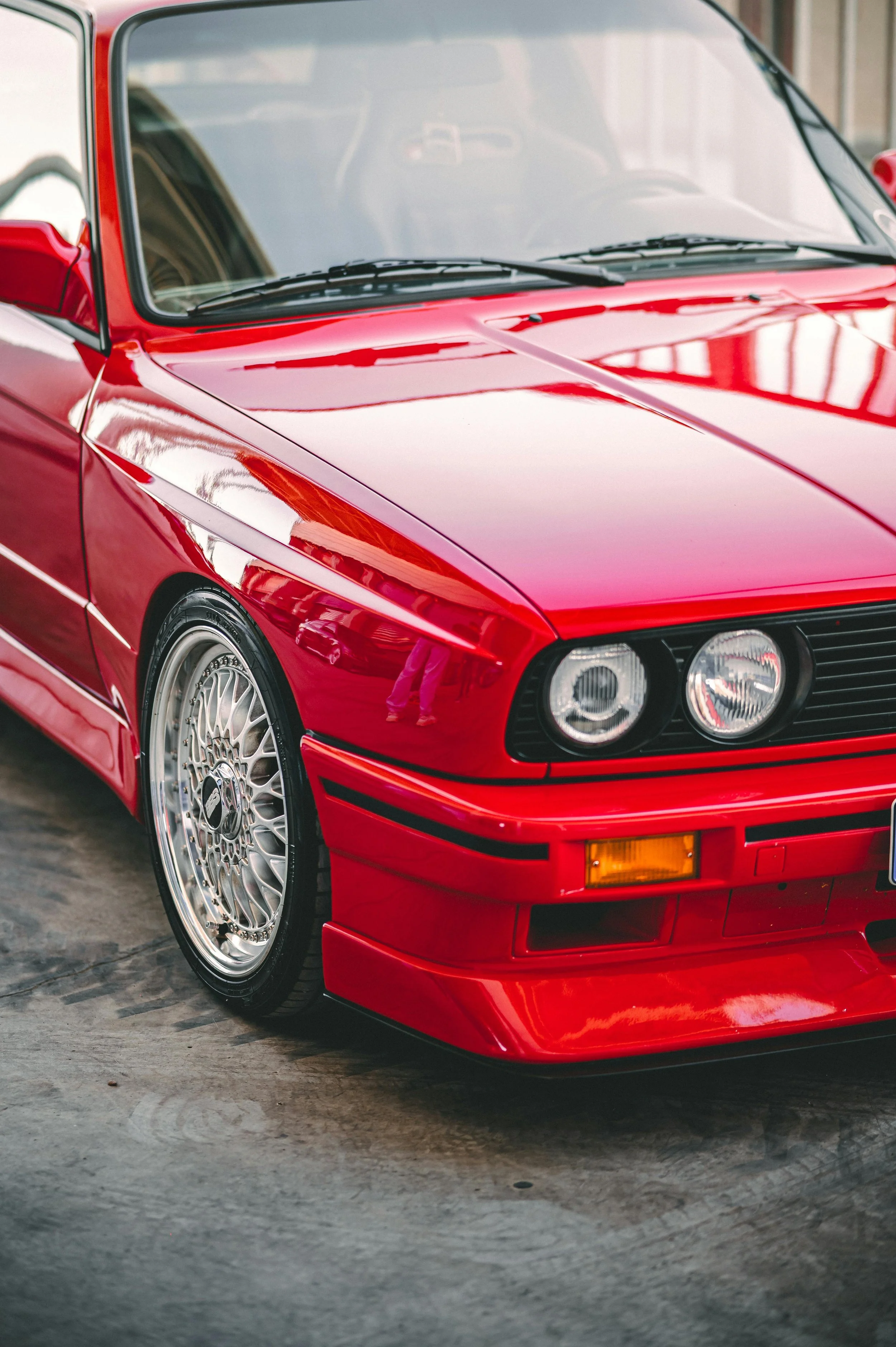 Close-up of a red classic sports car, showing the front left side, headlight, and wheel.