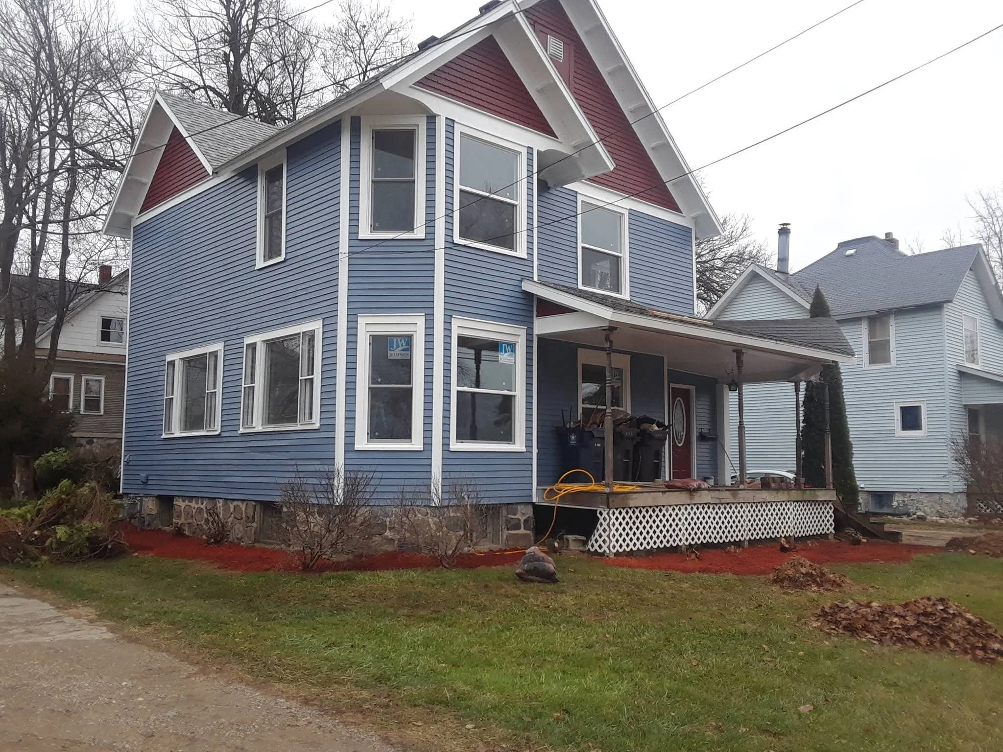 Blue two-story house with red trim, front porch, and ongoing yard work with dirt patches and grass.