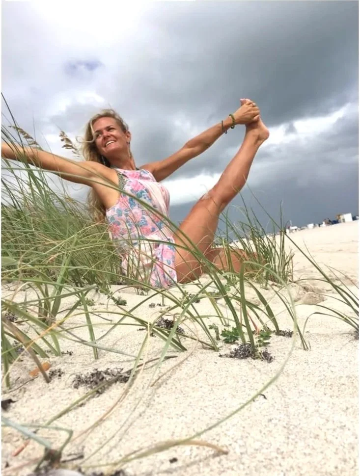 Leslie Storms doing yoga on a sandy beach, with tall grasses in foreground and dark clouds in the sky.