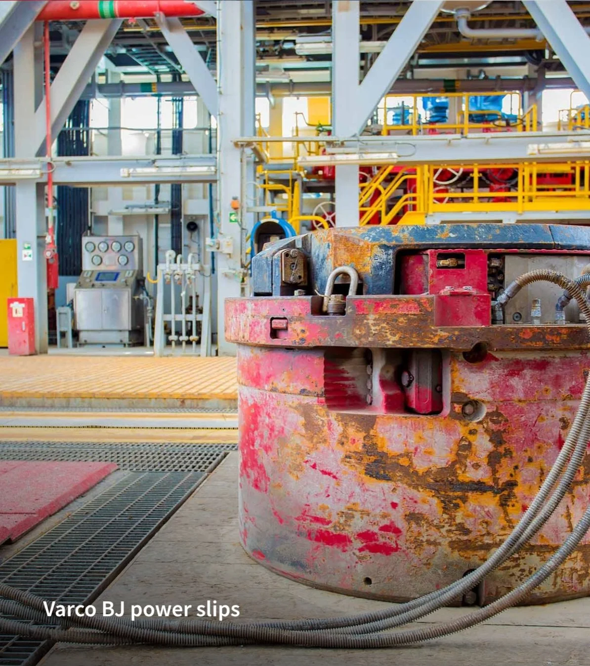 Industrial equipment and machinery on an oil or gas drilling platform, with a red and black surface in the foreground and yellow and blue guardrails in the background.