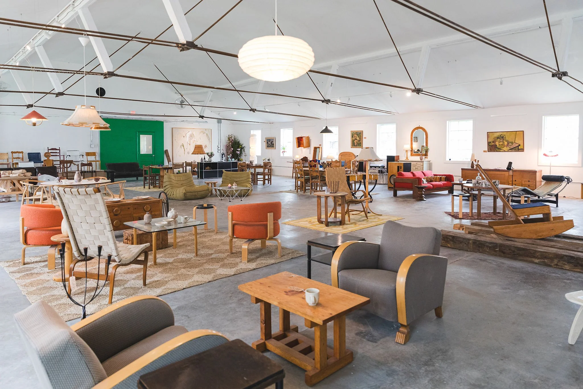 Spacious, well-lit room filled with various types of furniture, including chairs, sofas, tables, and decorative items, creating a cozy, eclectic living space or showroom.