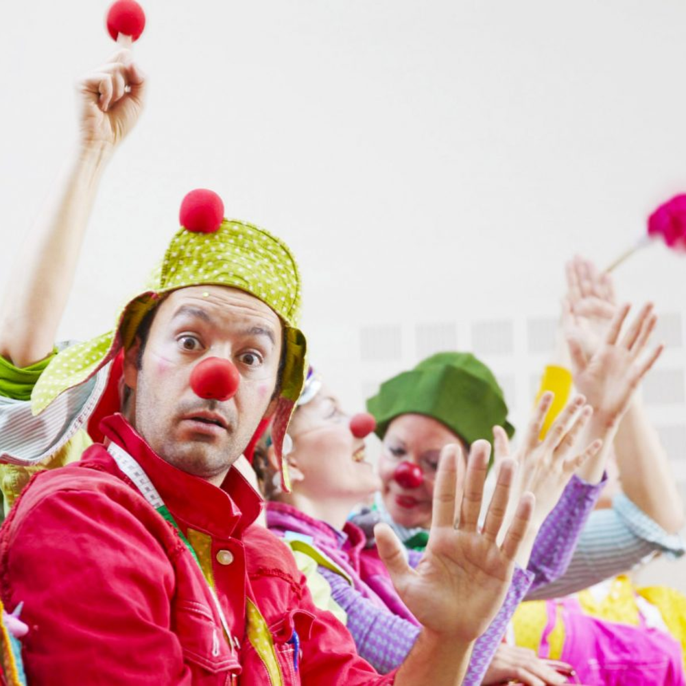 A man with dark curly hair, glasses, and a beard looking to the side in a light-colored room with a plant in the background.