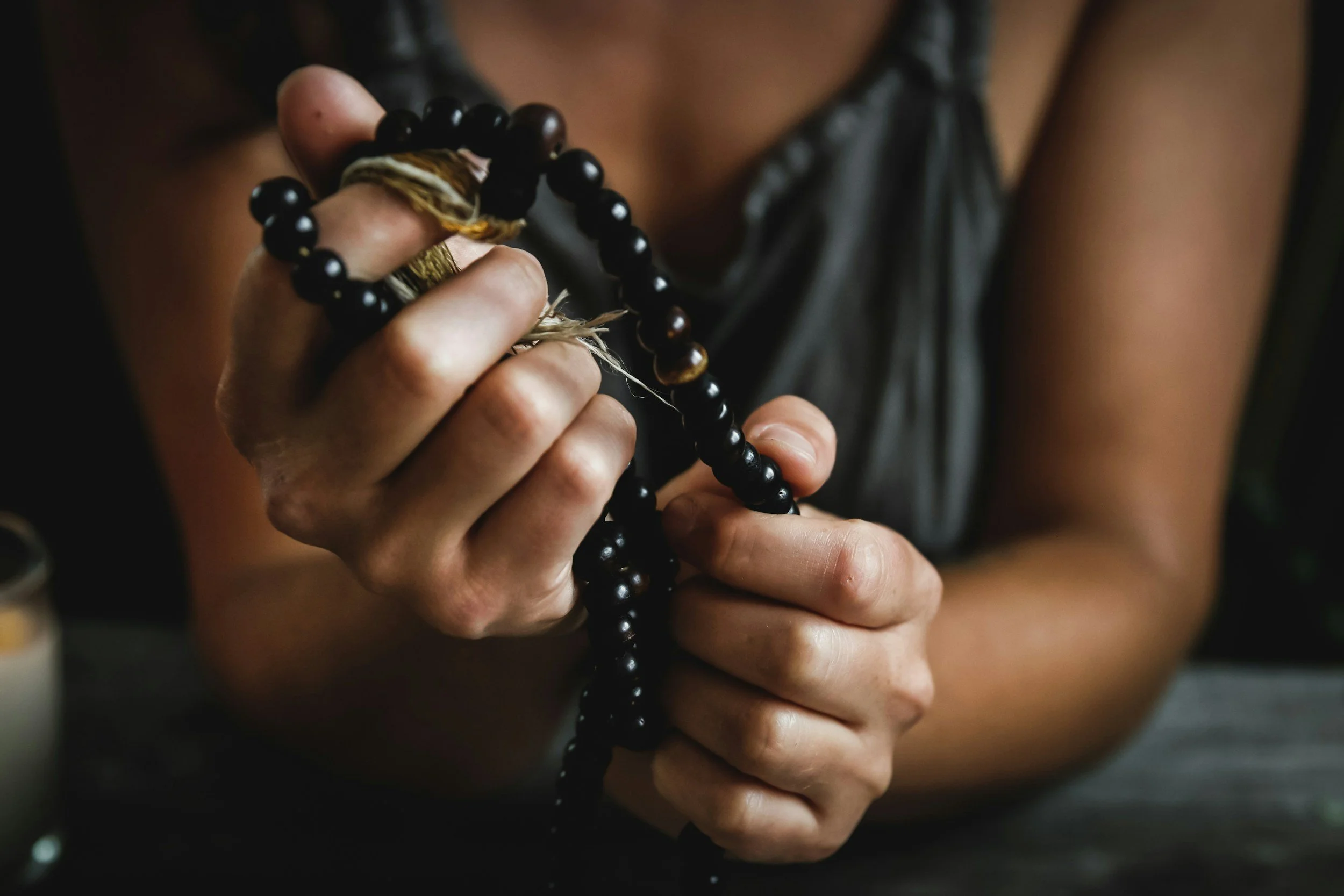 A person holding black prayer beads and a small wrapped object.
