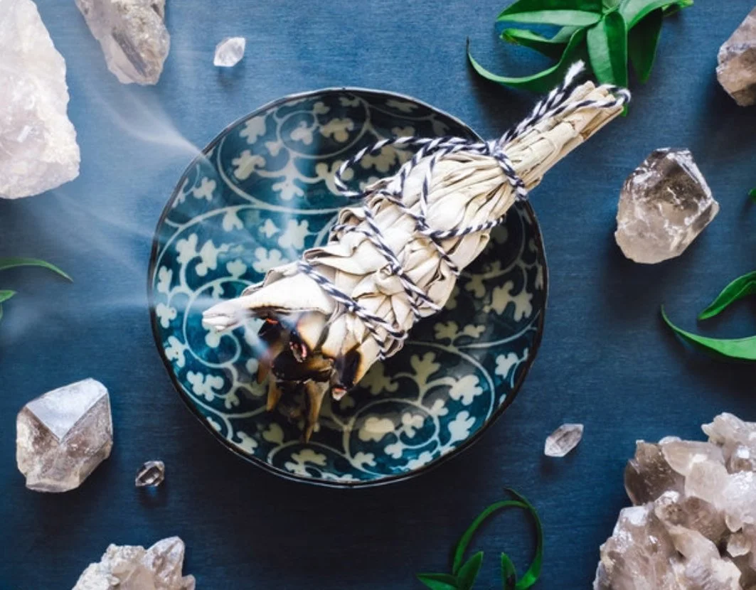 A ceramic dish with a blue and white pattern holding a bundle of shrimp wrapped in a cloth, surrounded by rocks and green leaves on a blue surface.