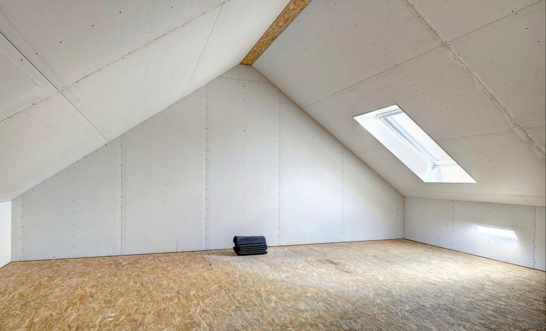 Leeg afgewerkt zolderkamer met geïnstalleerde ramen en houten vloer.