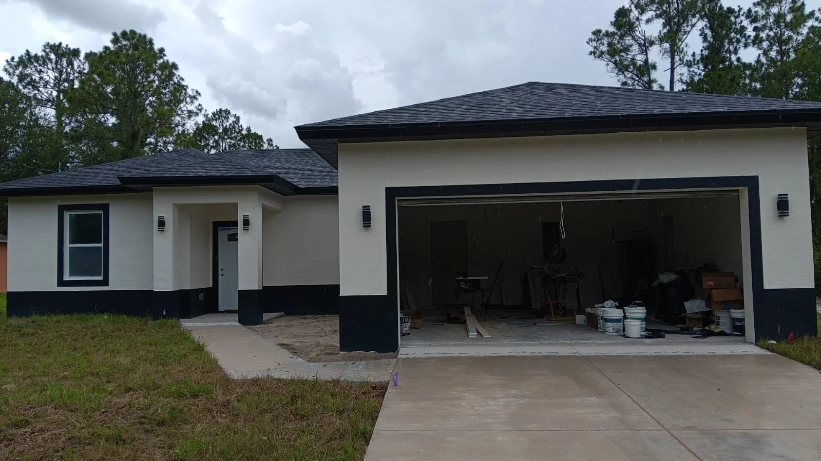 Newly constructed house with a front yard, a window, and an open garage filled with construction tools and supplies.