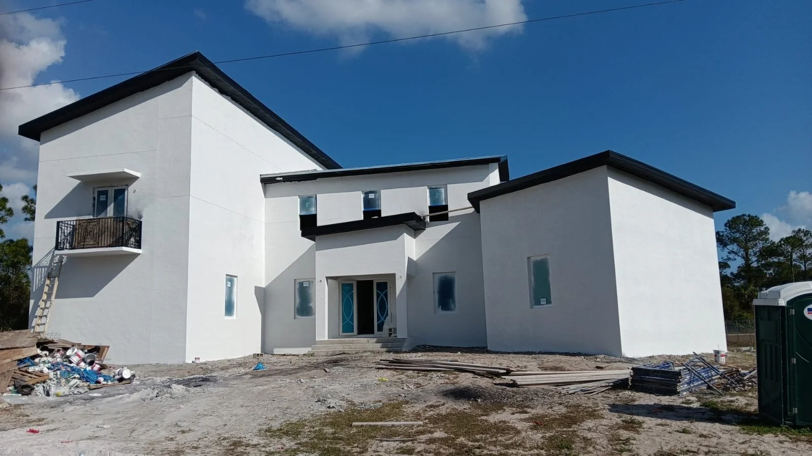 Newly constructed modern white house with black accents, surrounded by construction materials, under a blue sky.