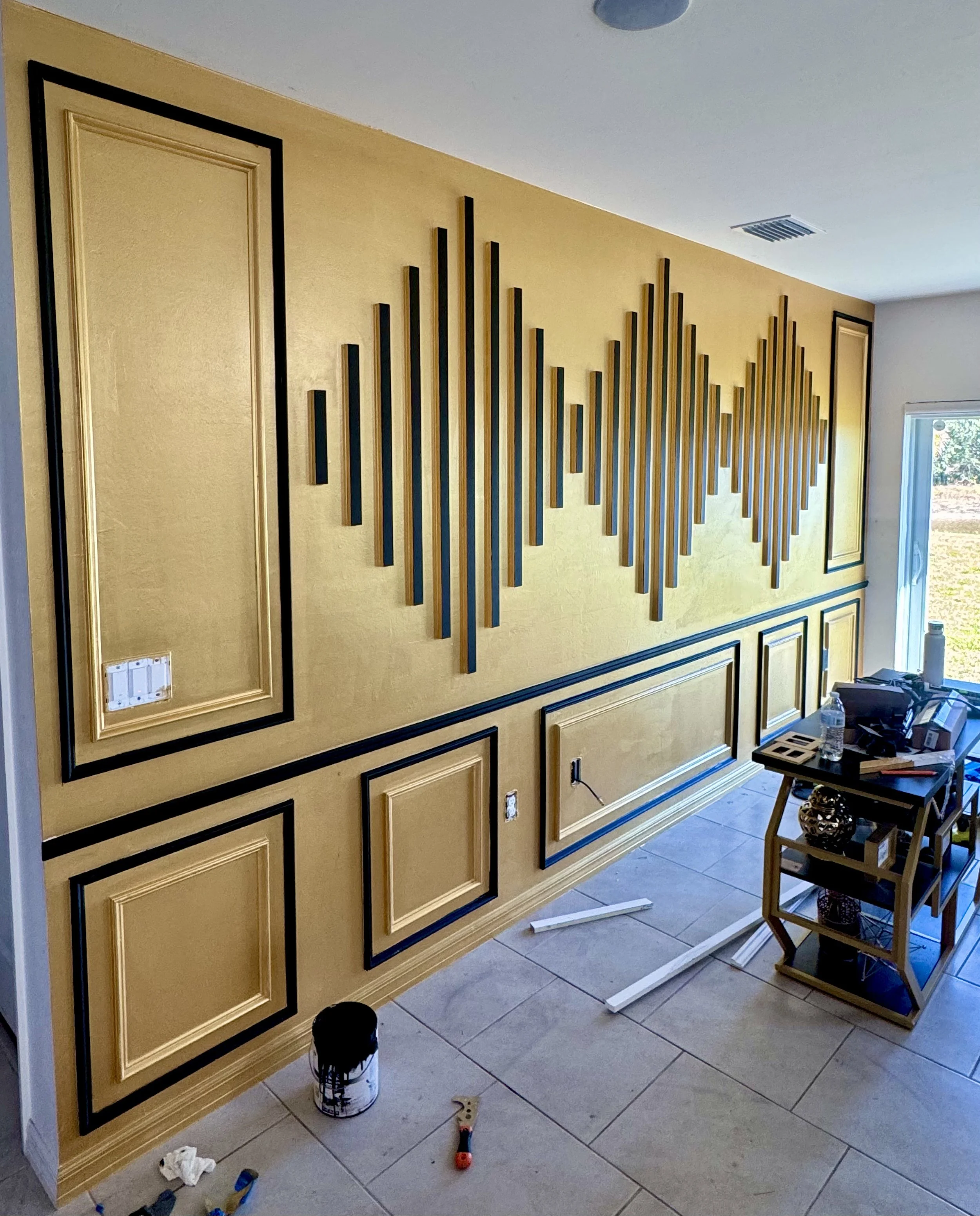 Interior wall with geometric 3D panel design, painted gray, with tiled flooring and electrical outlet.