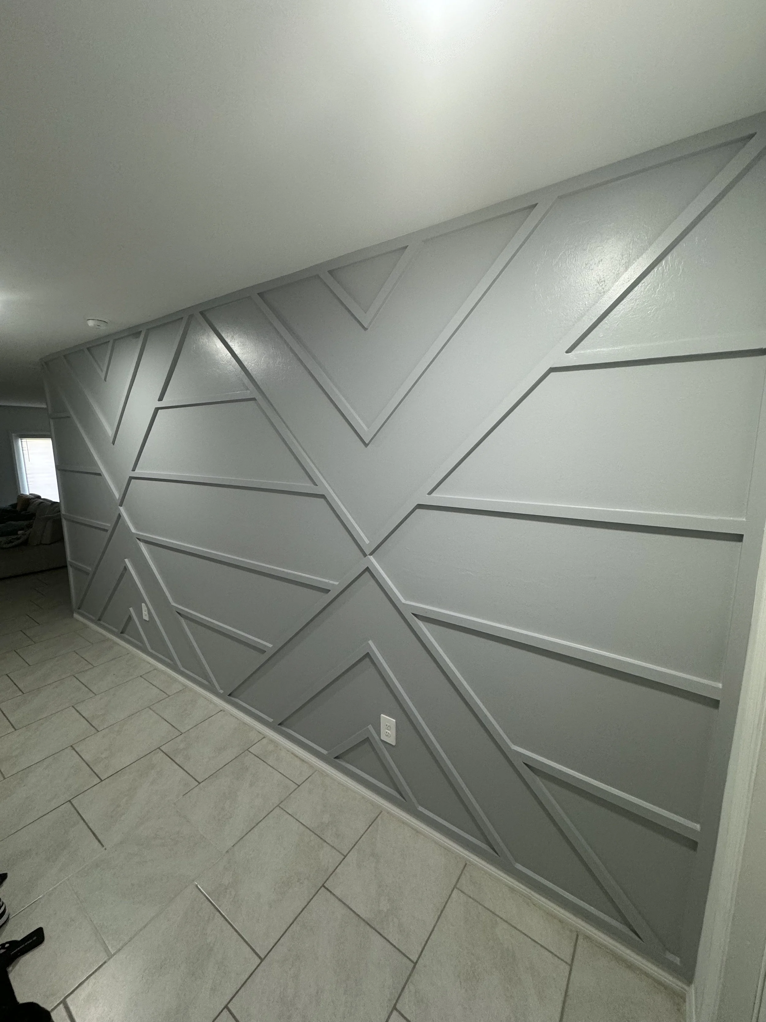 Interior wall with geometric 3D wall panel design in gray, near tiled floor, in a modern home.