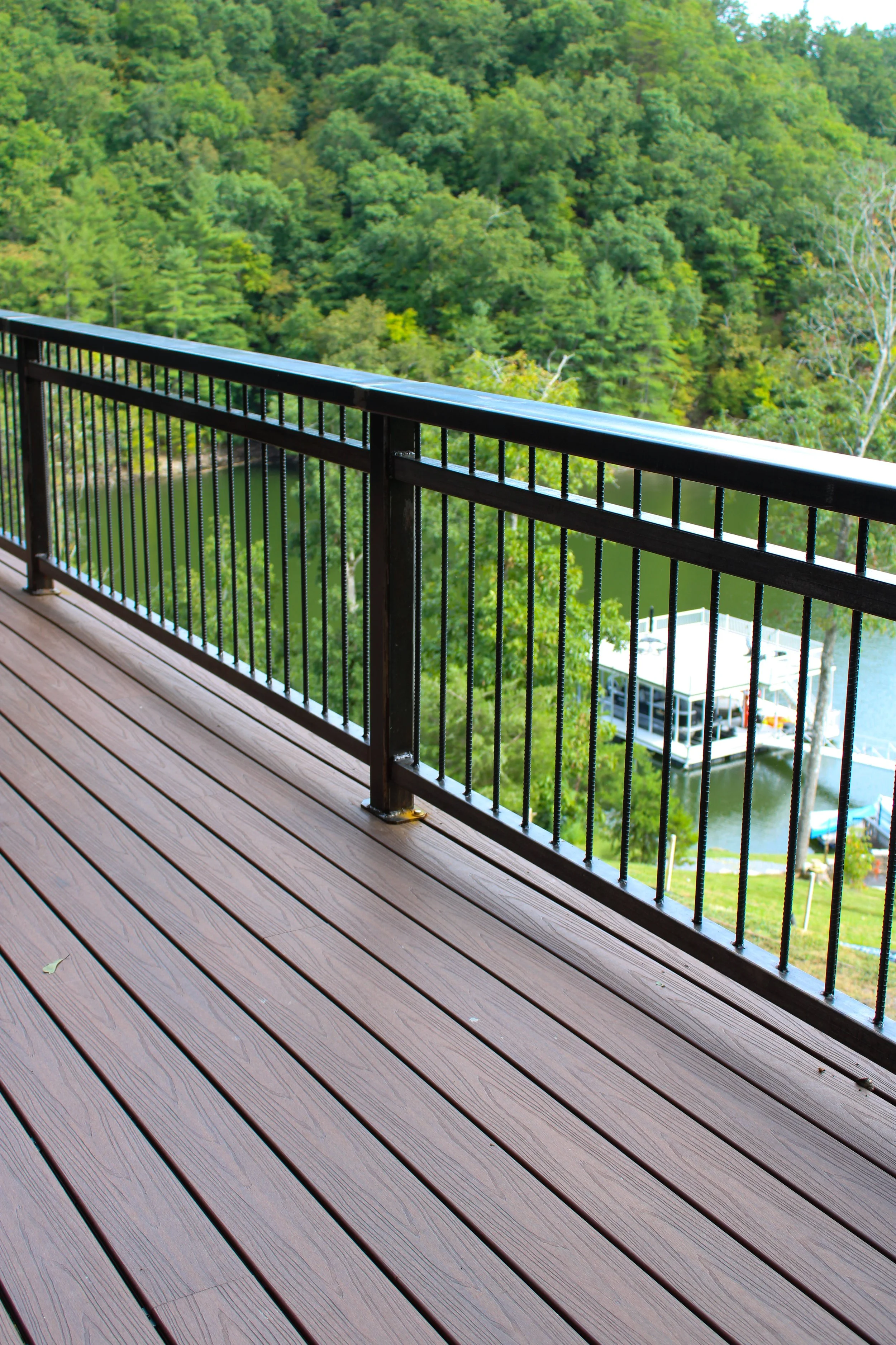 A wooden deck with a metal railing overlooking a green, tree-filled landscape and a waterway below.