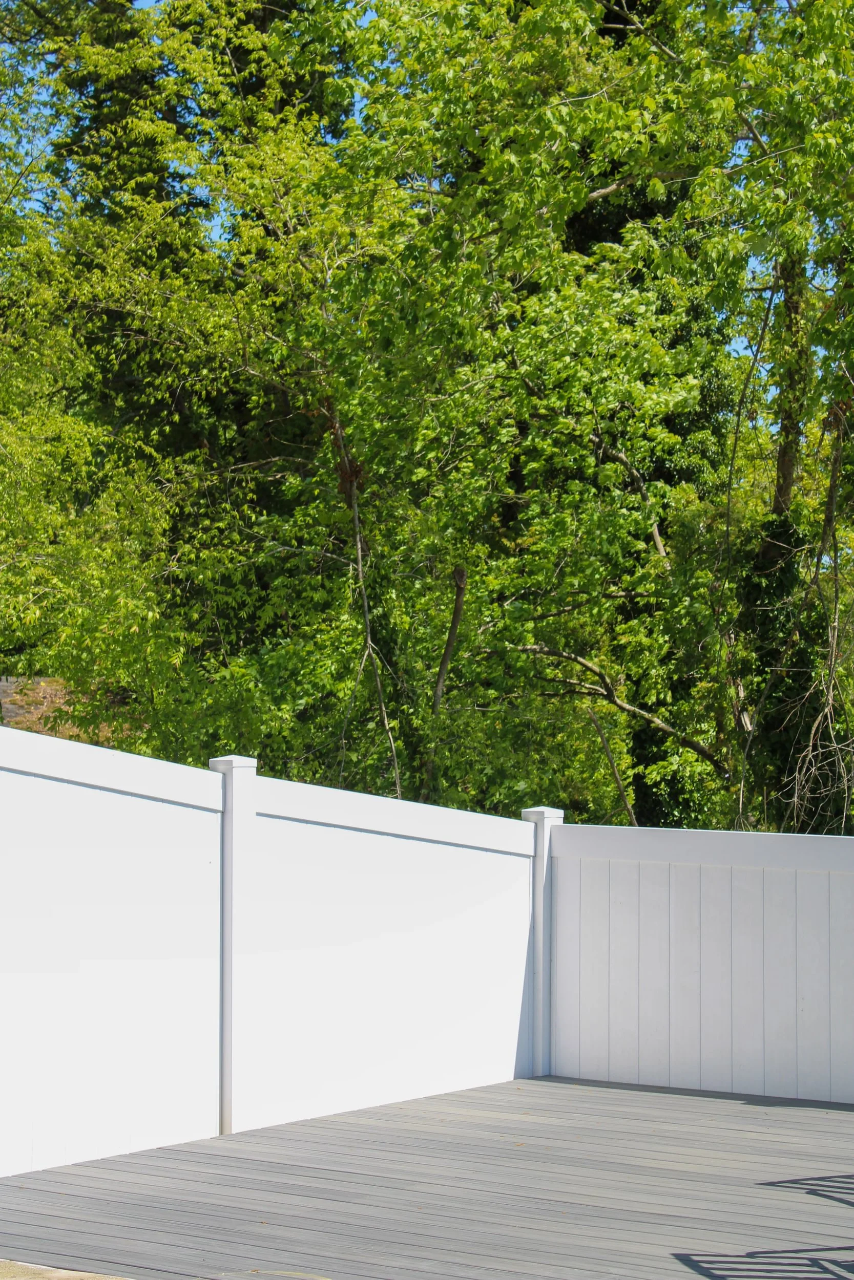 A backyard deck with a white fence and a background of large green trees under a clear blue sky.