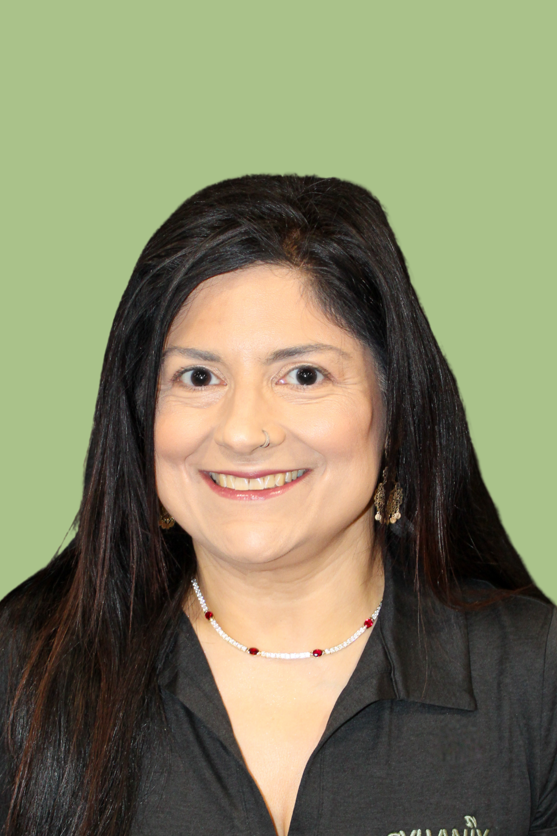 A woman with long dark hair, wearing a black shirt and jewelry, smiling against a light green background.