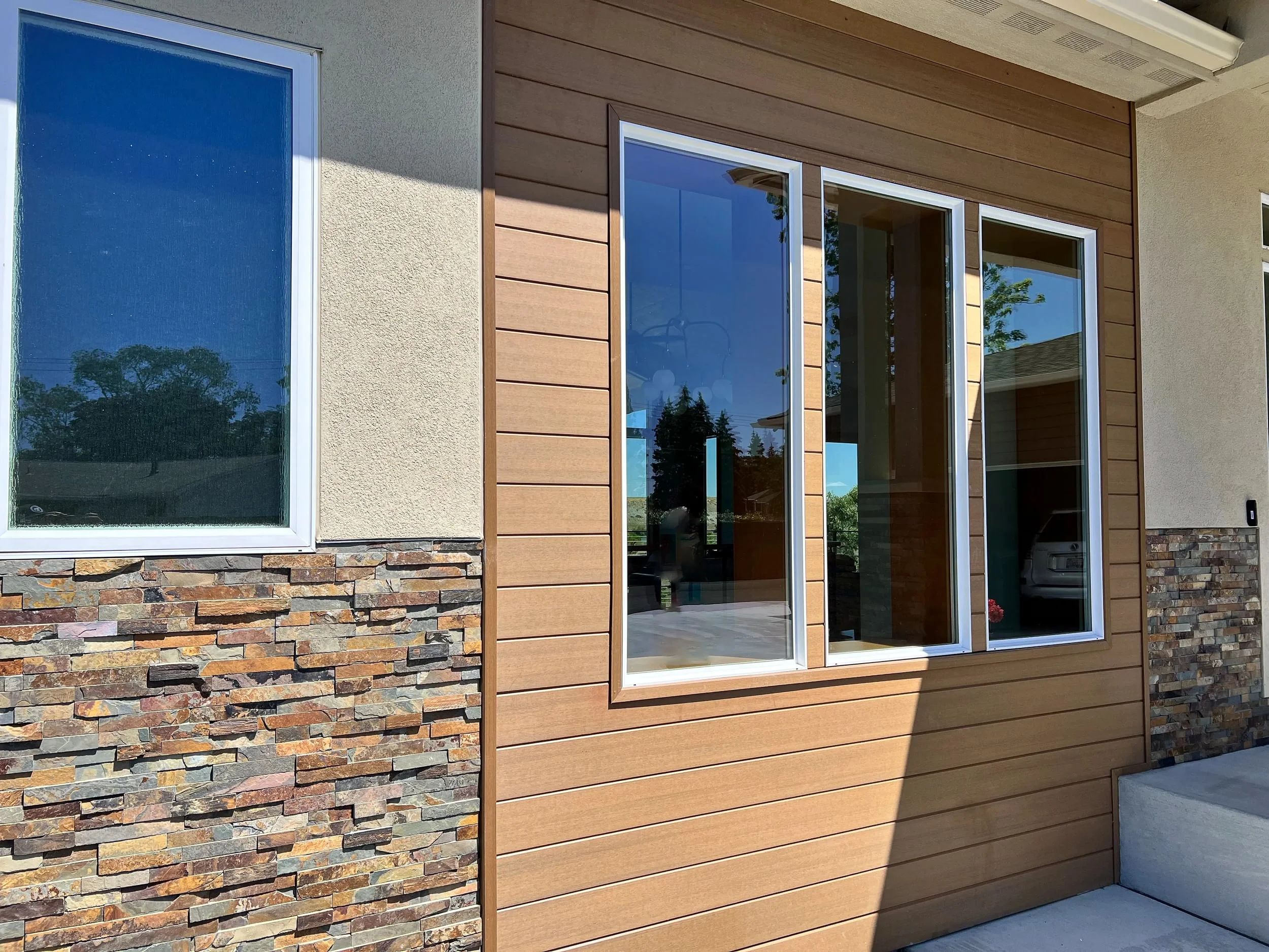Close-up view of a house exterior with a window on the left and sliding glass doors on the right, featuring a wood siding and stone foundation.