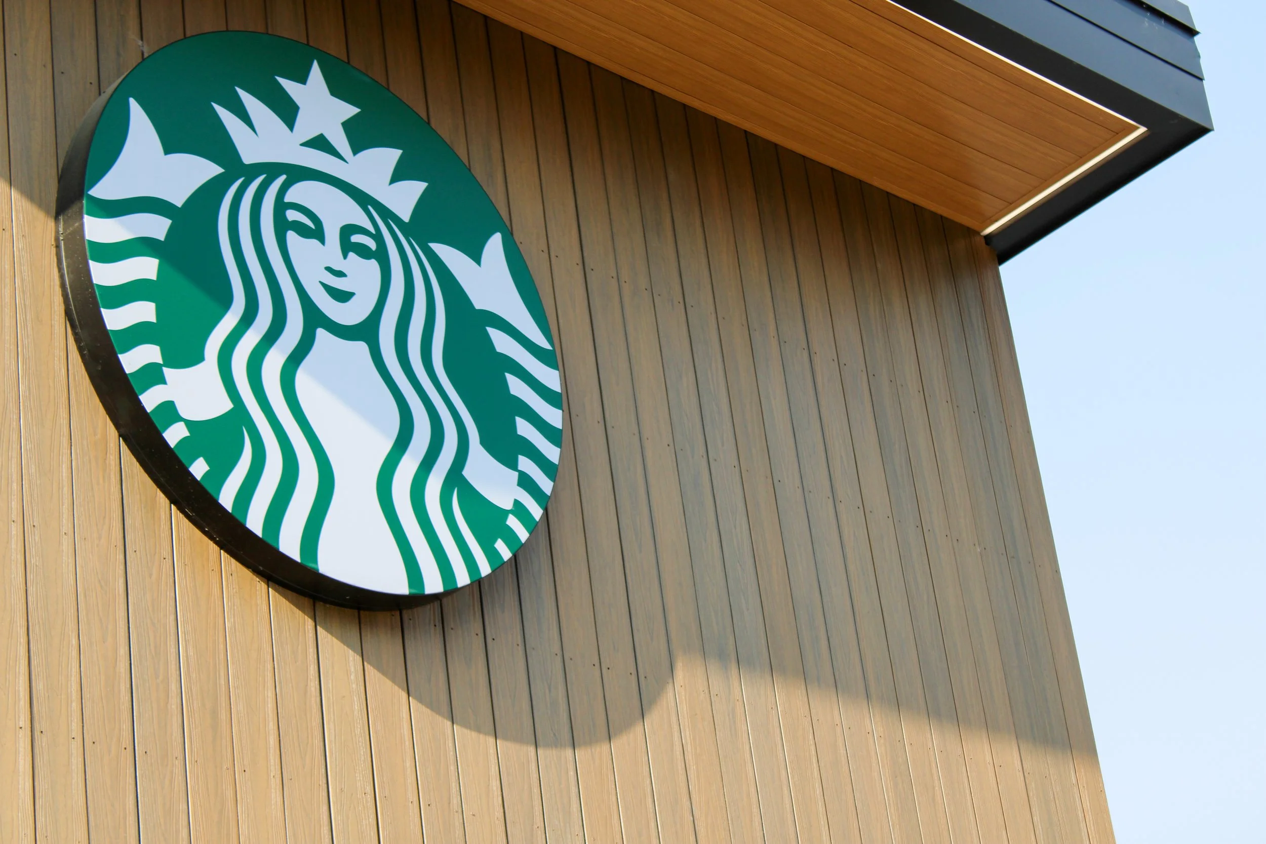 Starbucks logo on the exterior wall of a building with wood paneling and a section of the roof visible.