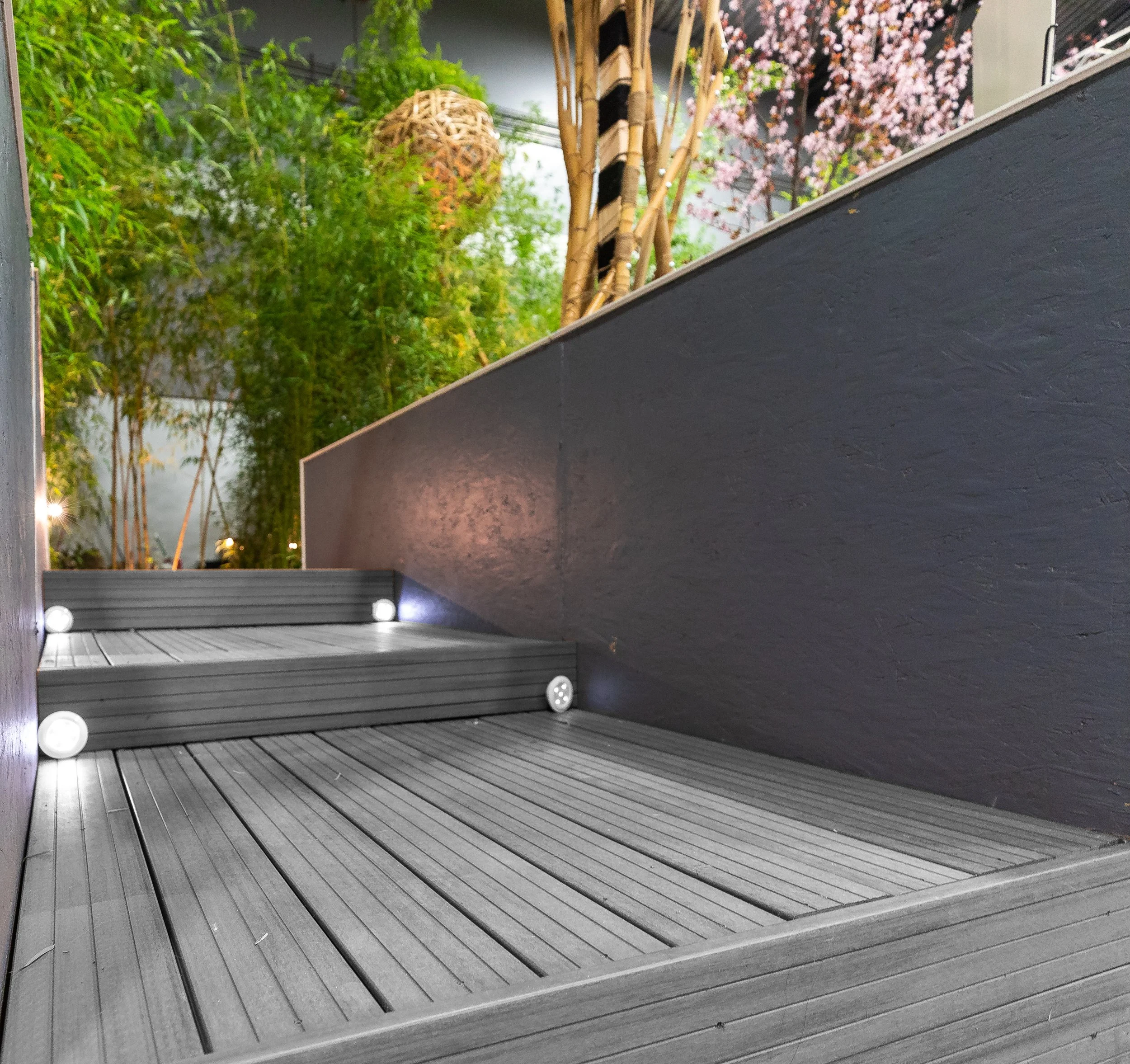 Modern entrance with steps, black wall, and tree with pink flowers visible in the background.