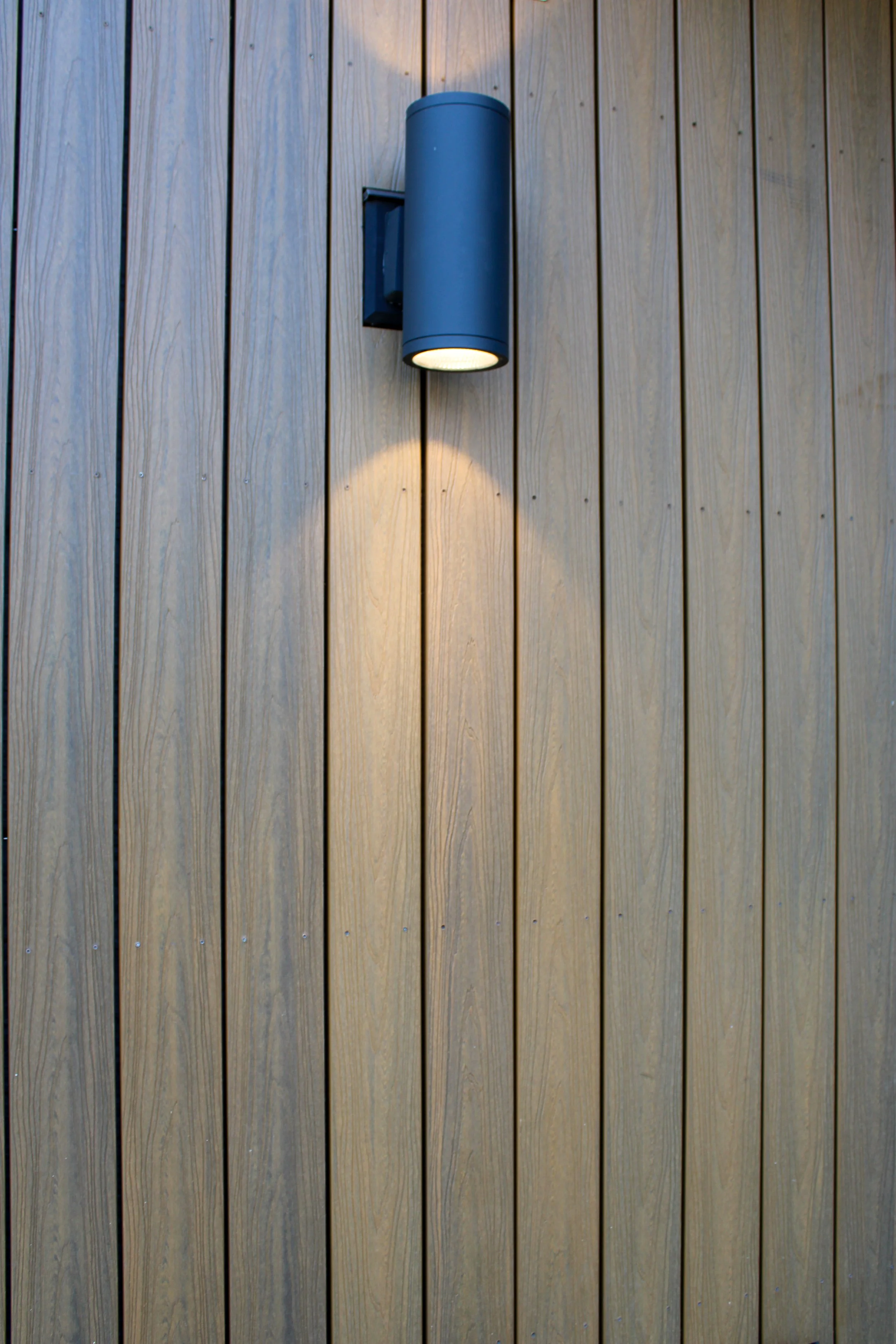 A modern wall-mounted outdoor light fixture on a wooden wall with vertical planks.