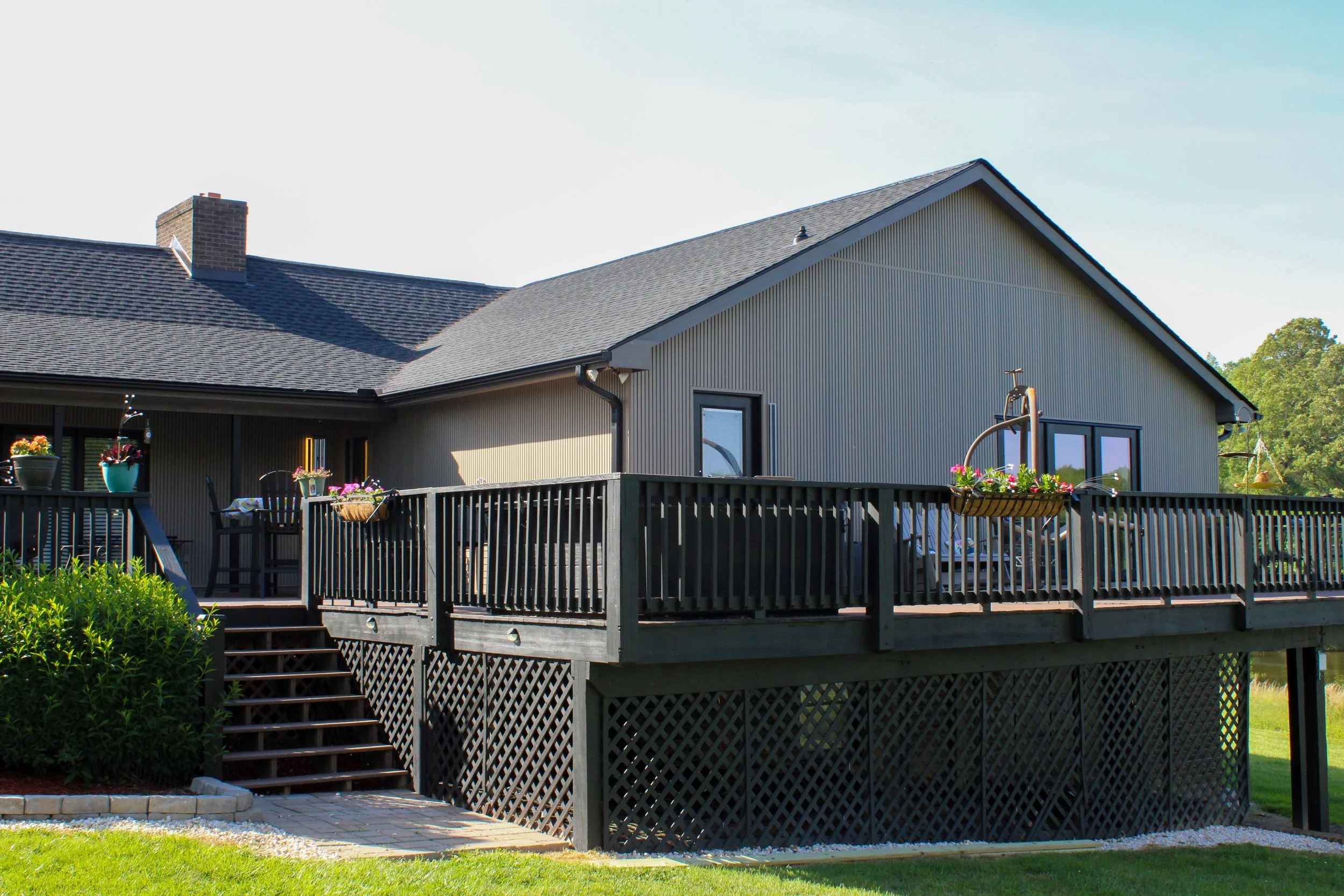 Backyard view of a house with a deck, plants, flowers, and a grassy lawn.