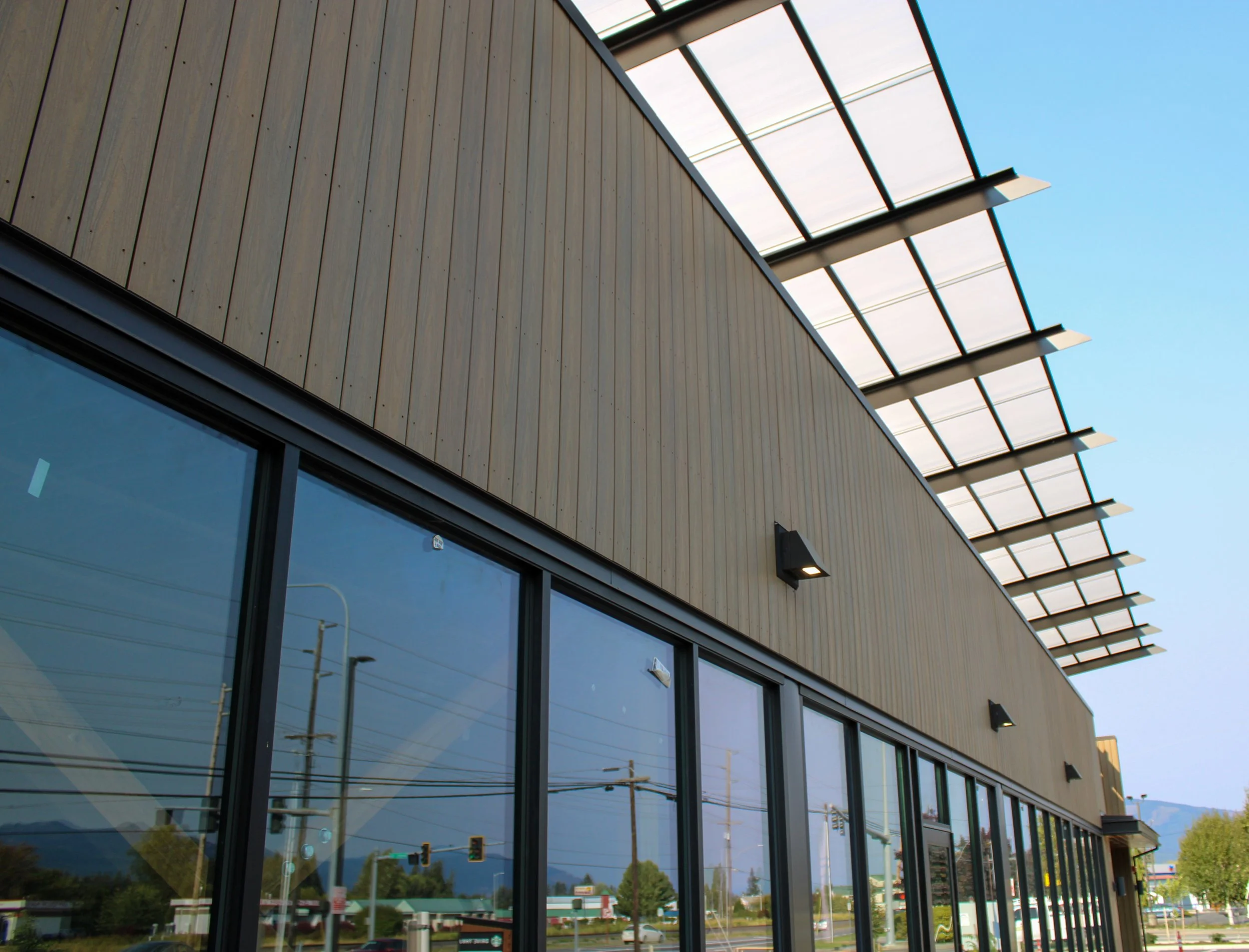 Modern building with large reflective glass windows and wooden paneling on the exterior, with solar panels on the roof and a clear blue sky in the background.