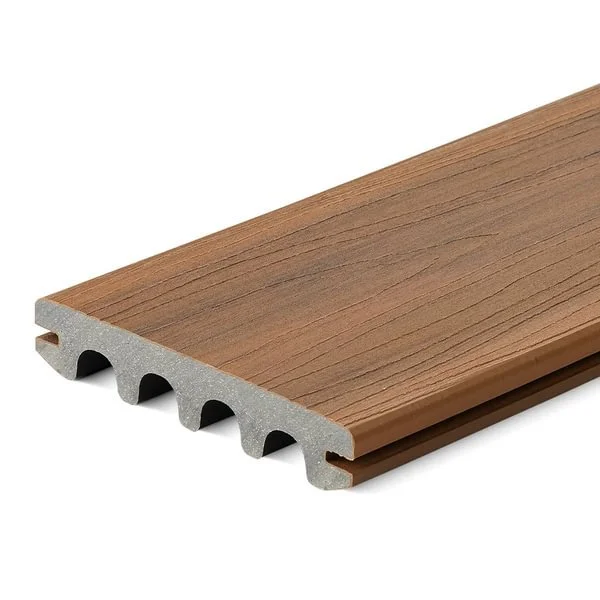 A piece of composite decking board with a wood-like surface and a gray underside with hollow channels.