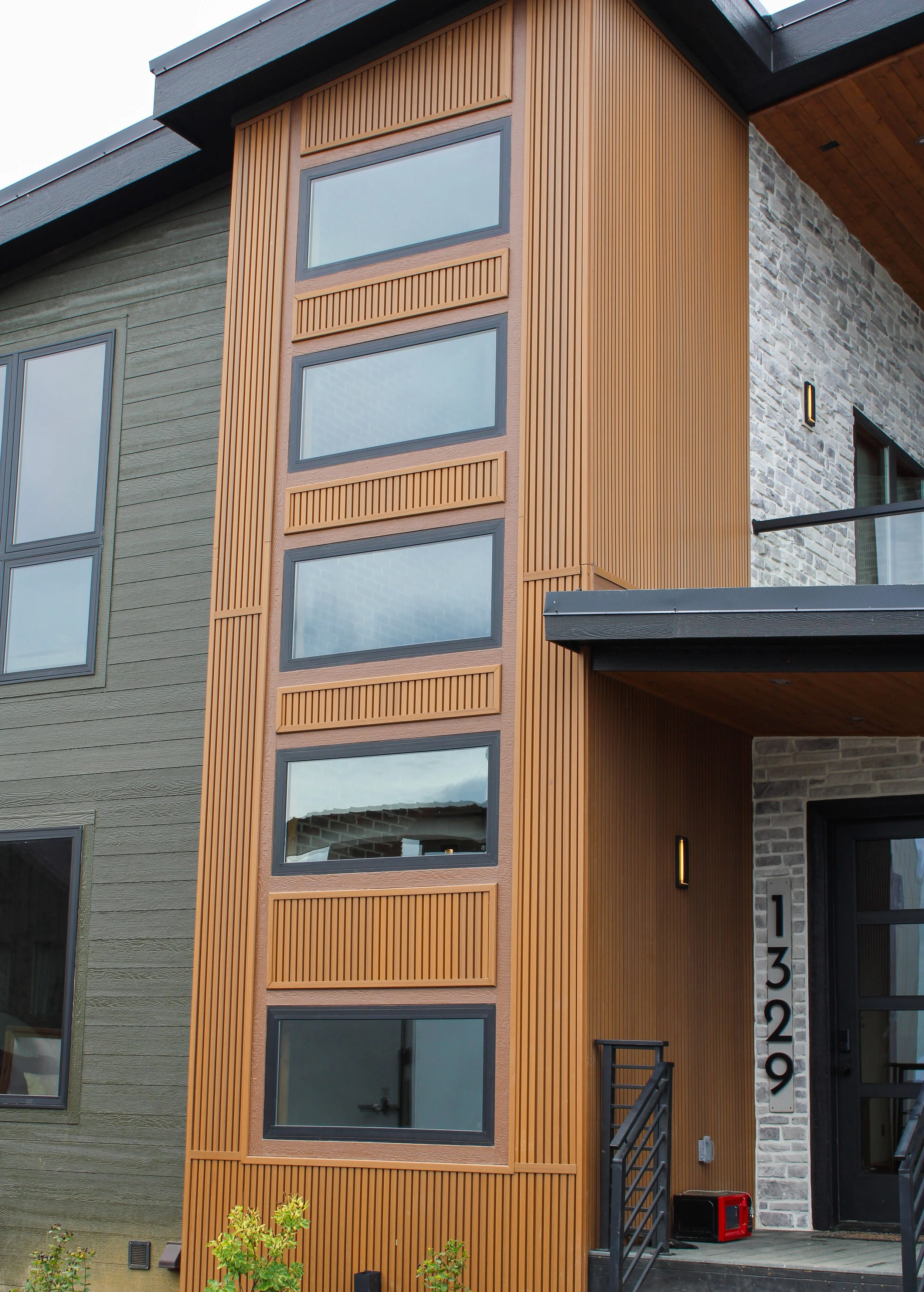 Modern multi-story building with green, wood, and brick exterior, large windows, and black stairs.
