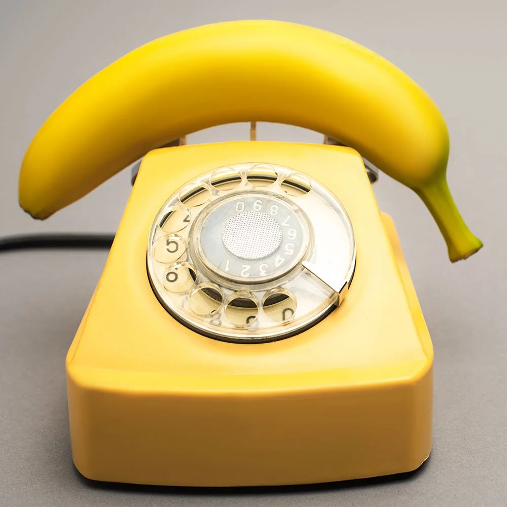 A vintage yellow rotary telephone with a banana placed on top of it.