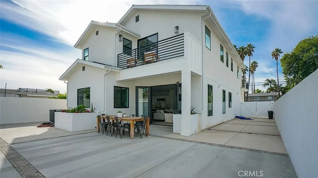 Modern two-story white house with patio and outdoor dining area, surrounded by a concrete yard.