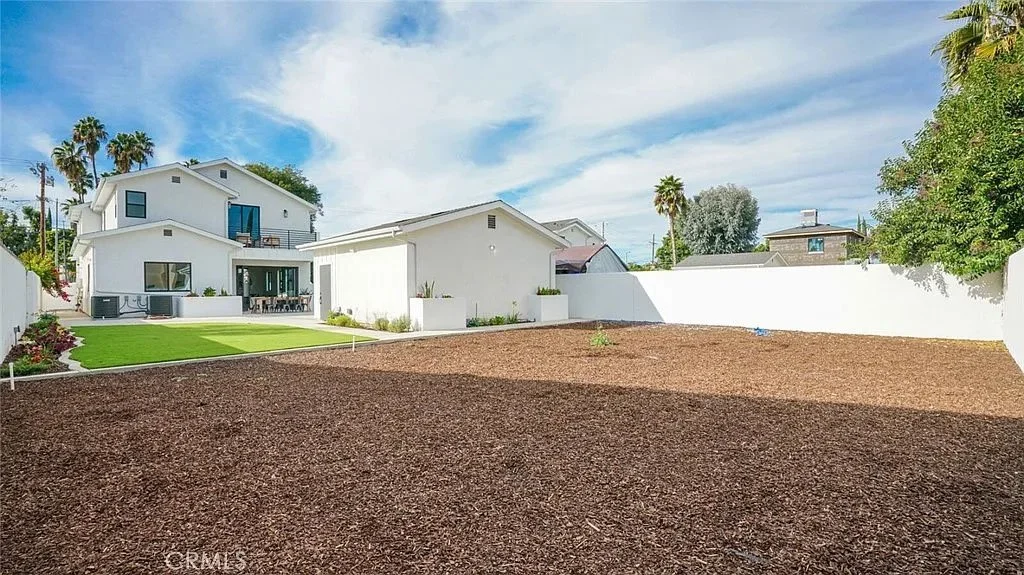 Backyard view of modern two-story house with a landscaped lawn, white exterior walls, and surrounding trees.