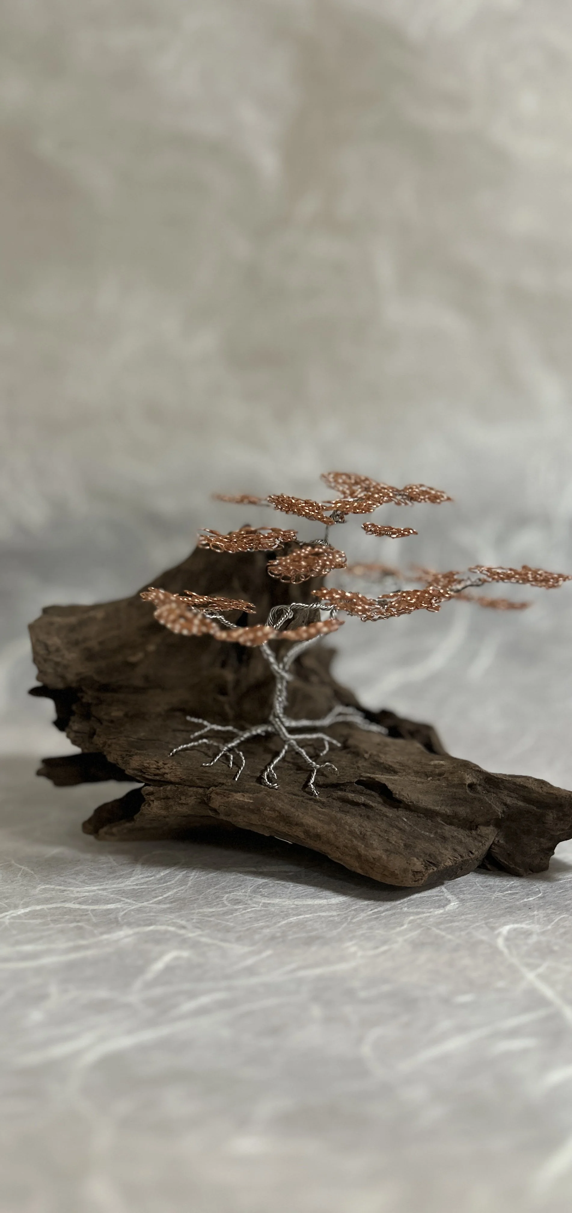 A decorative wire tree sculpture with copper leaves, mounted on a piece of driftwood.