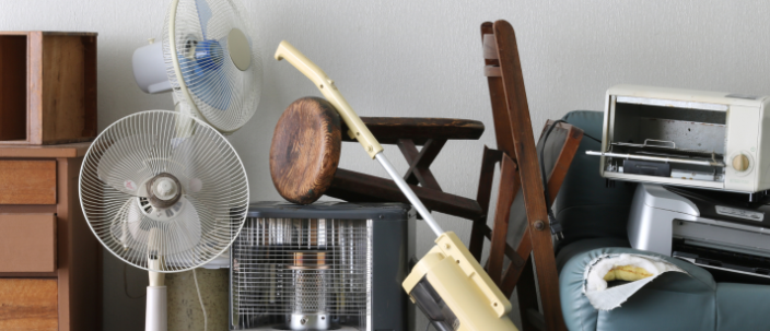 Cluttered room with three standing fans, a wooden and metal chair, a small heater, a vacuum cleaner, and a printer on a blue sofa, against a white wall.