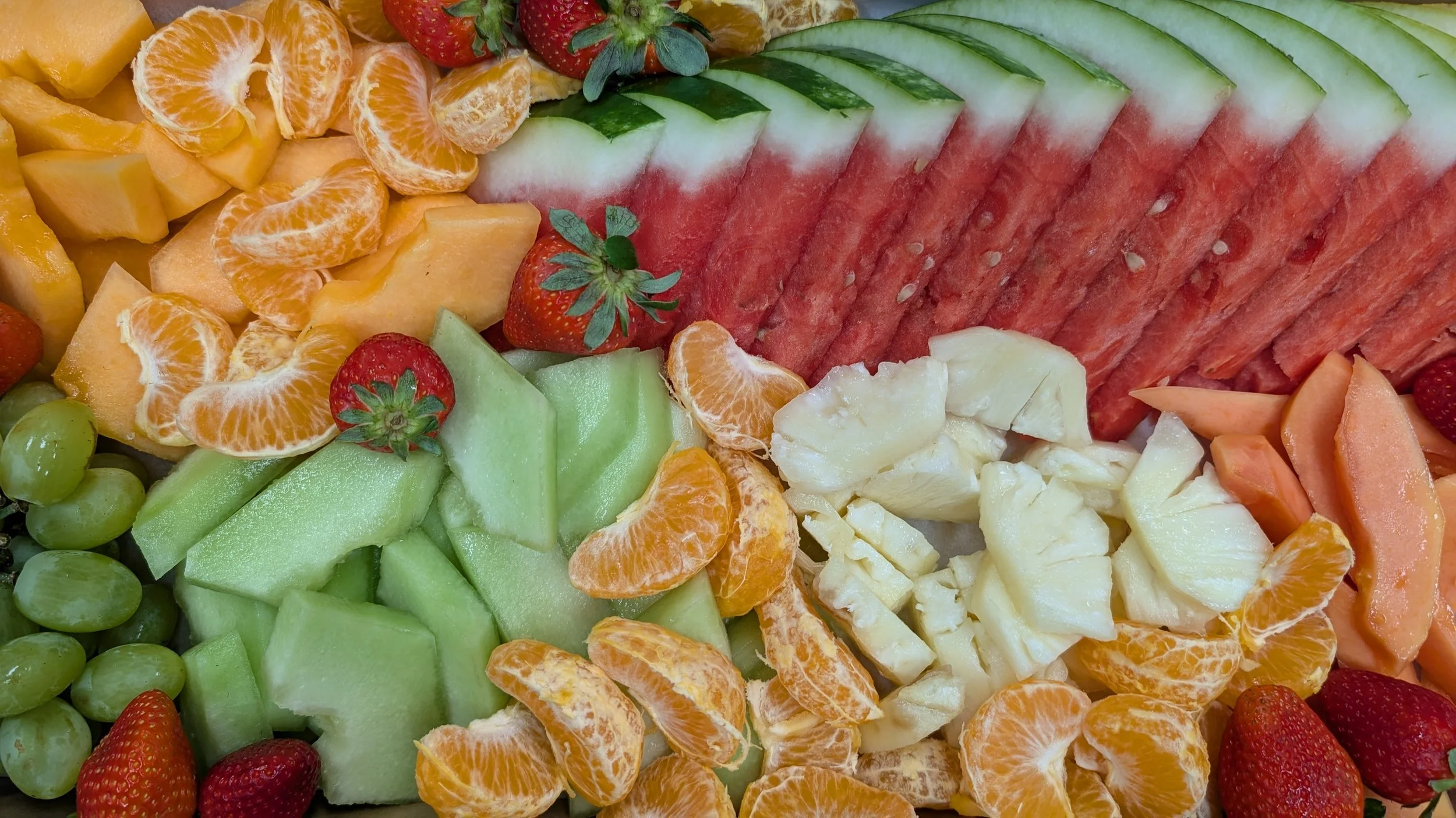 A colorful assortment of sliced fruits including watermelon, honeydew, cantaloupe, strawberries, strawberries, grapes, oranges, and other mixed fruits.