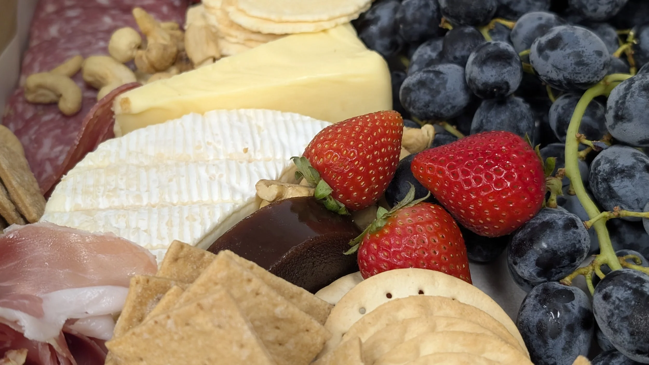 An assortment of cheese, strawberries, black grapes, crackers, and sliced meats arranged on a platter.