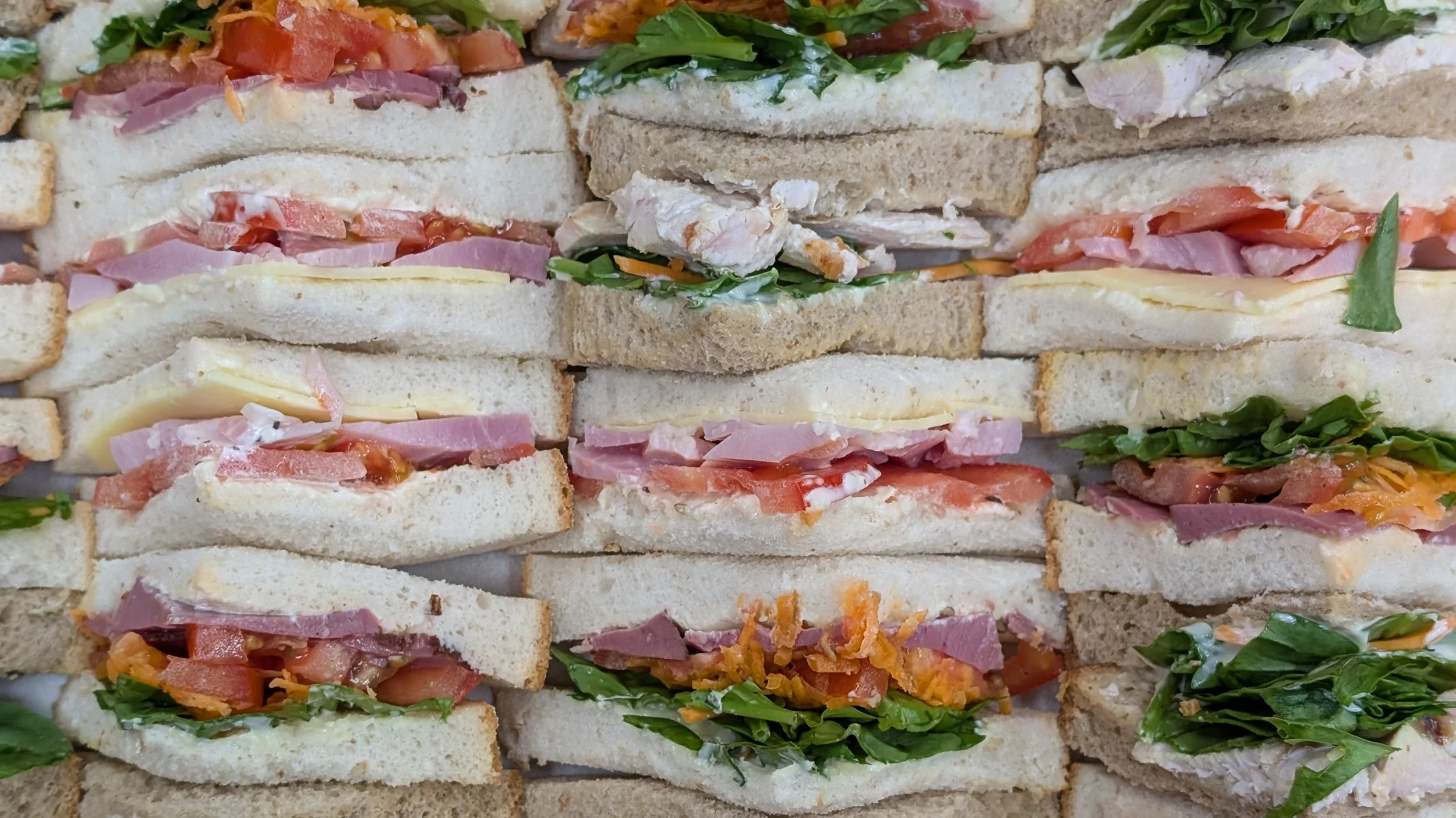 Assorted sandwiches with various meats, cheeses, and vegetables layered between slices of white and whole wheat bread.