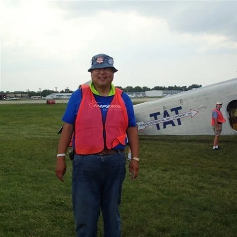 Alice Chen's father wearing a red vest and directing plane traffic at an air show, a vivid image from the personal history that grounds The Unlearning Studio's story