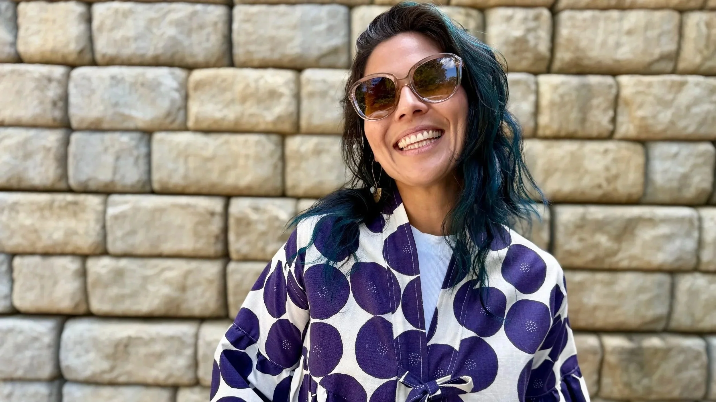 Alice Chen smiling in sunglasses and a purple anorak jacket, radiating the warmth, color and bold self-expression she brings to her coaching and facilitation work