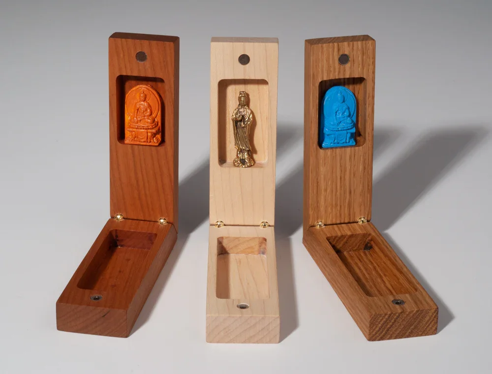 Three wooden boxes with carved statues inside, each box features a different colored statue and wood finish.