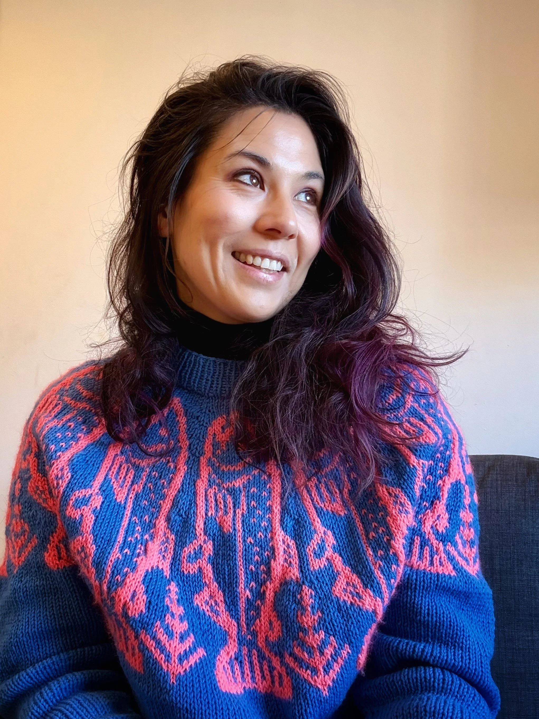 Alice Chen wearing a handknit periwinkle and salmon colored sweater featuring a salmon motif she knitted herself, a wearable expression of creativity and personal style