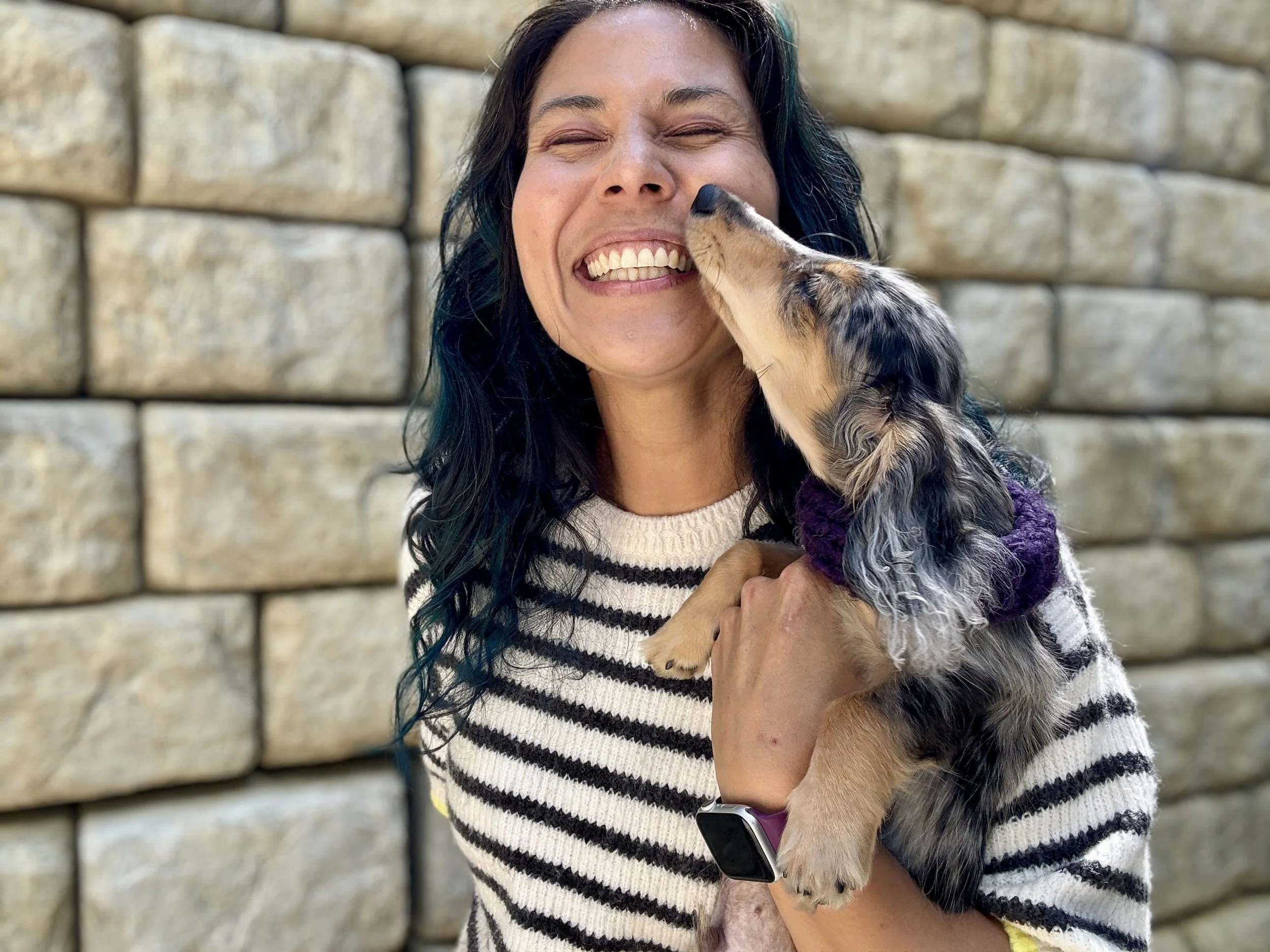 Alice Chen laughing as a dapple dachshund licks her face, capturing the playfulness, warmth and delight that she brings to The Unlearning Studio