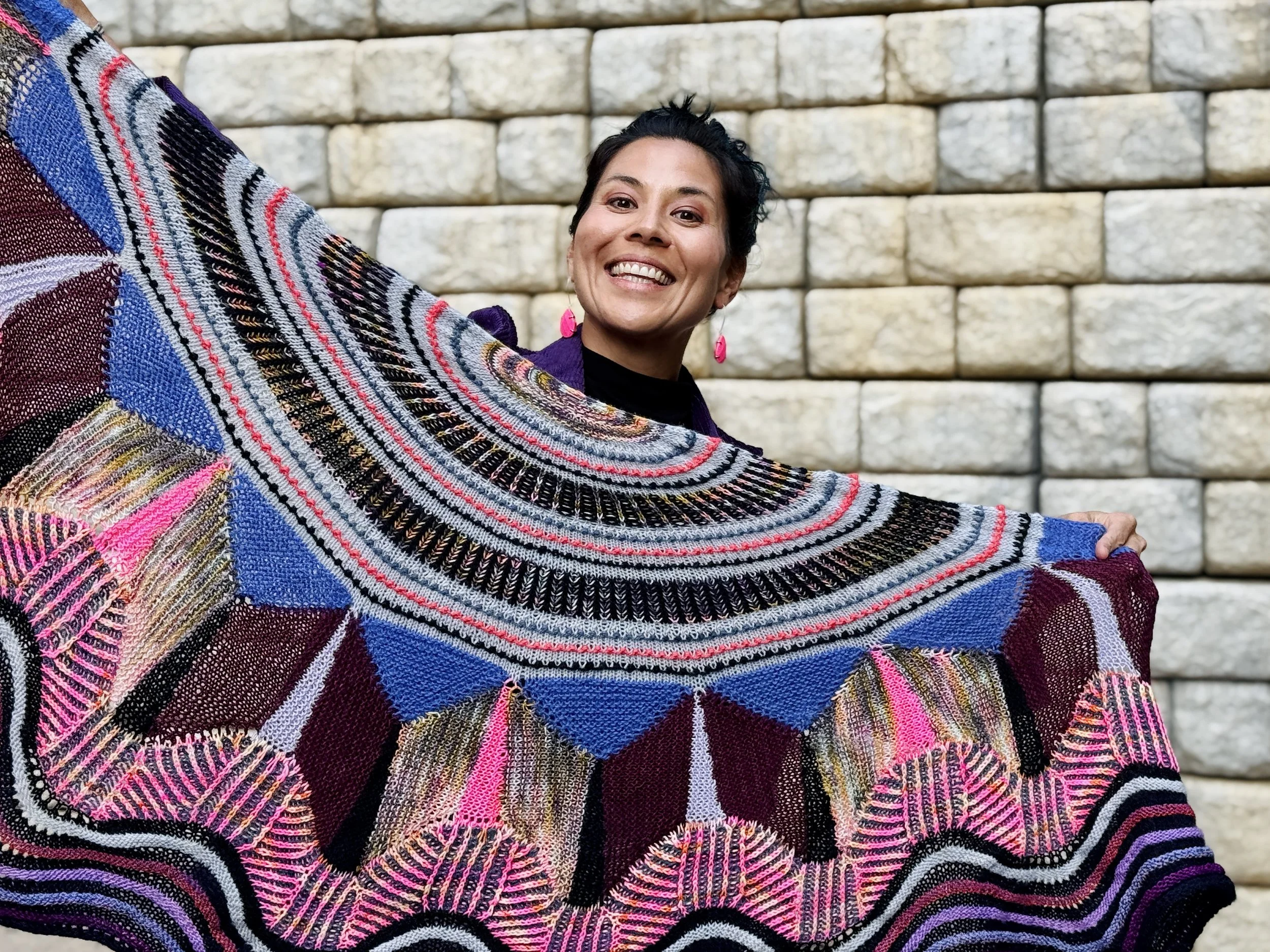 Alice Chen holding up a large, vibrantly colorful scarf she hand-knitted herself, expressing the creative spirit and joyful making that runs through everything at The Unlearning Studio