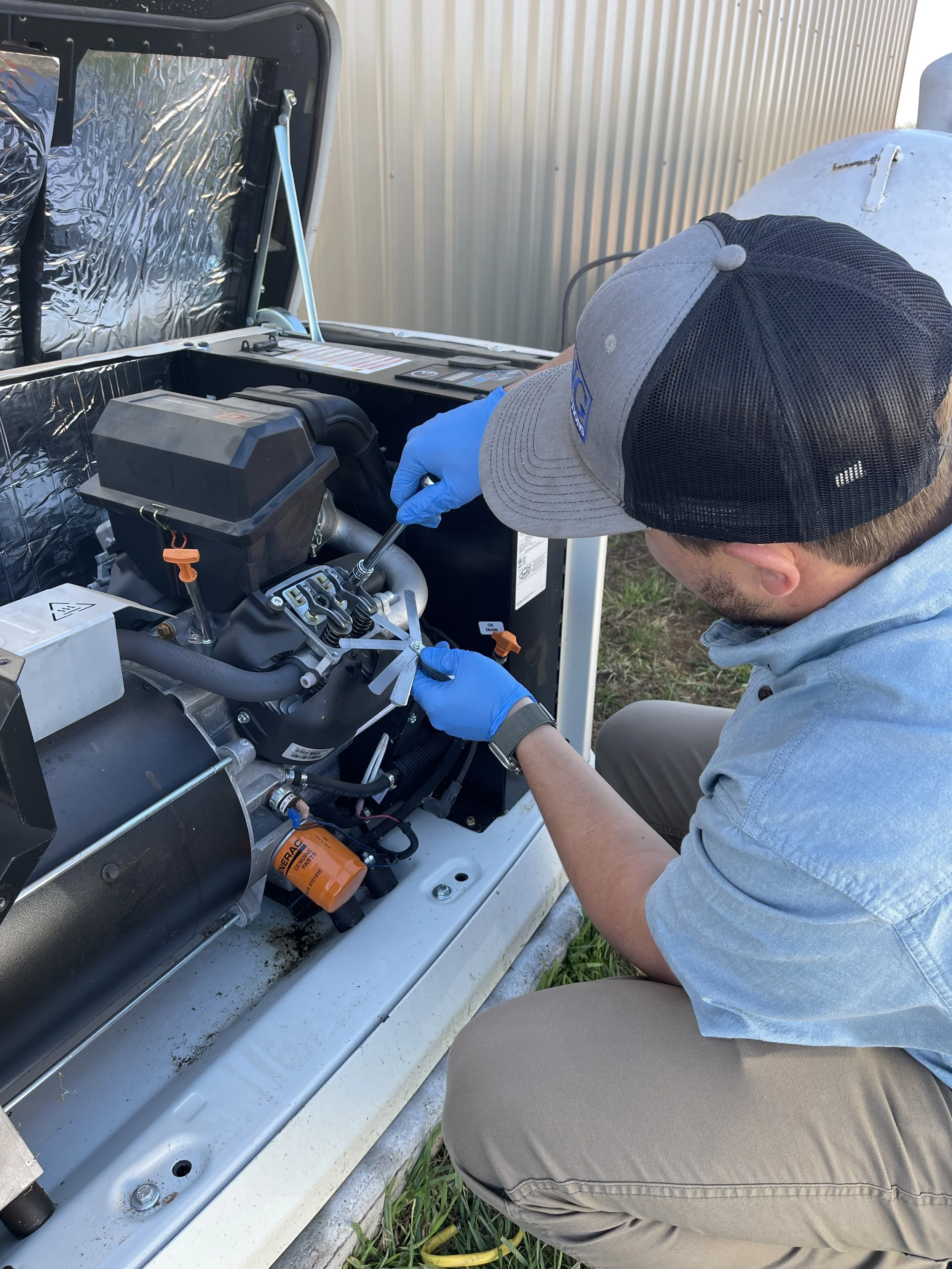 A technician wearing a cap, glasses, and gloves working on a generator or industrial equipment outdoors.