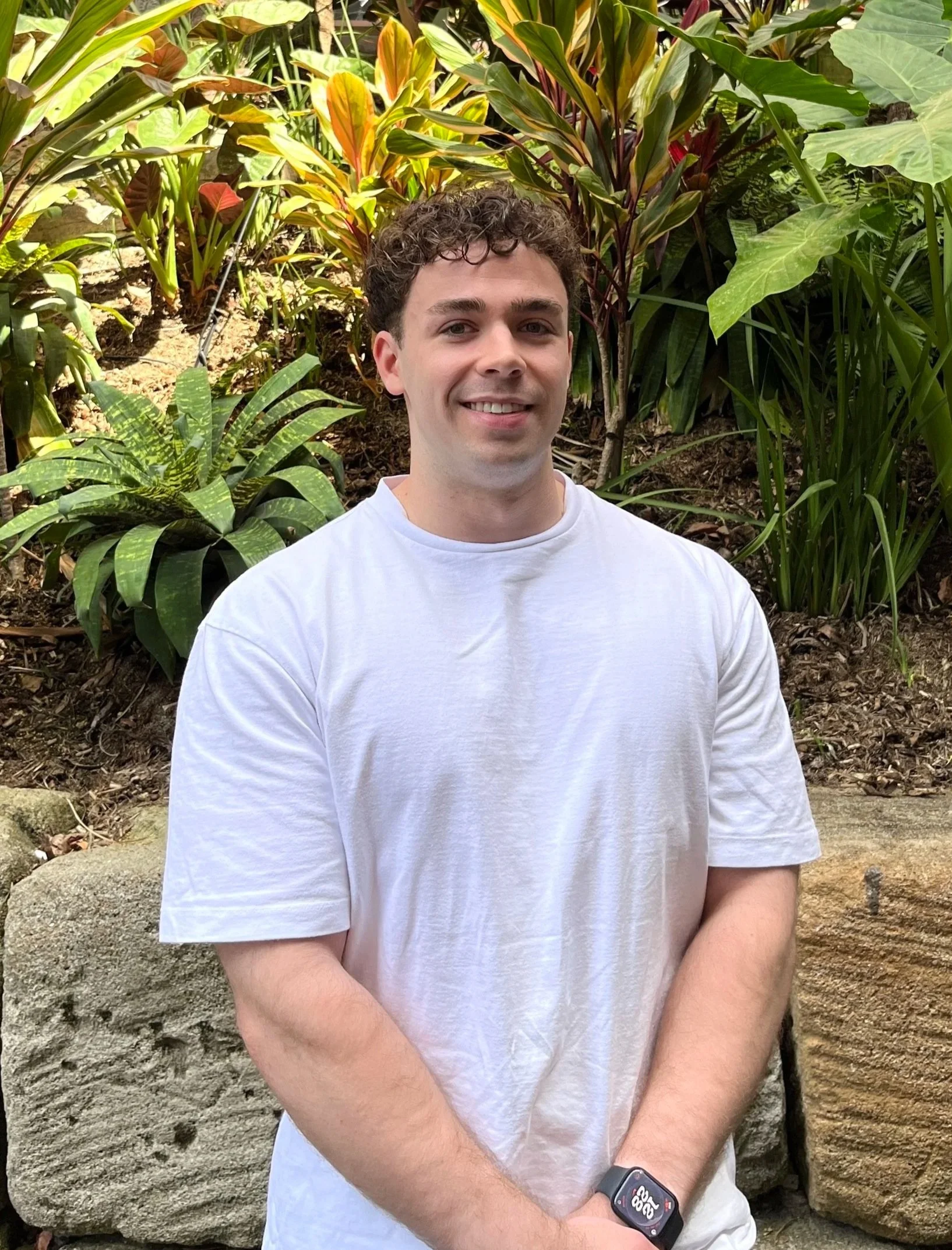 A young man with curly brown hair wearing a black polo shirt, standing against a white background.